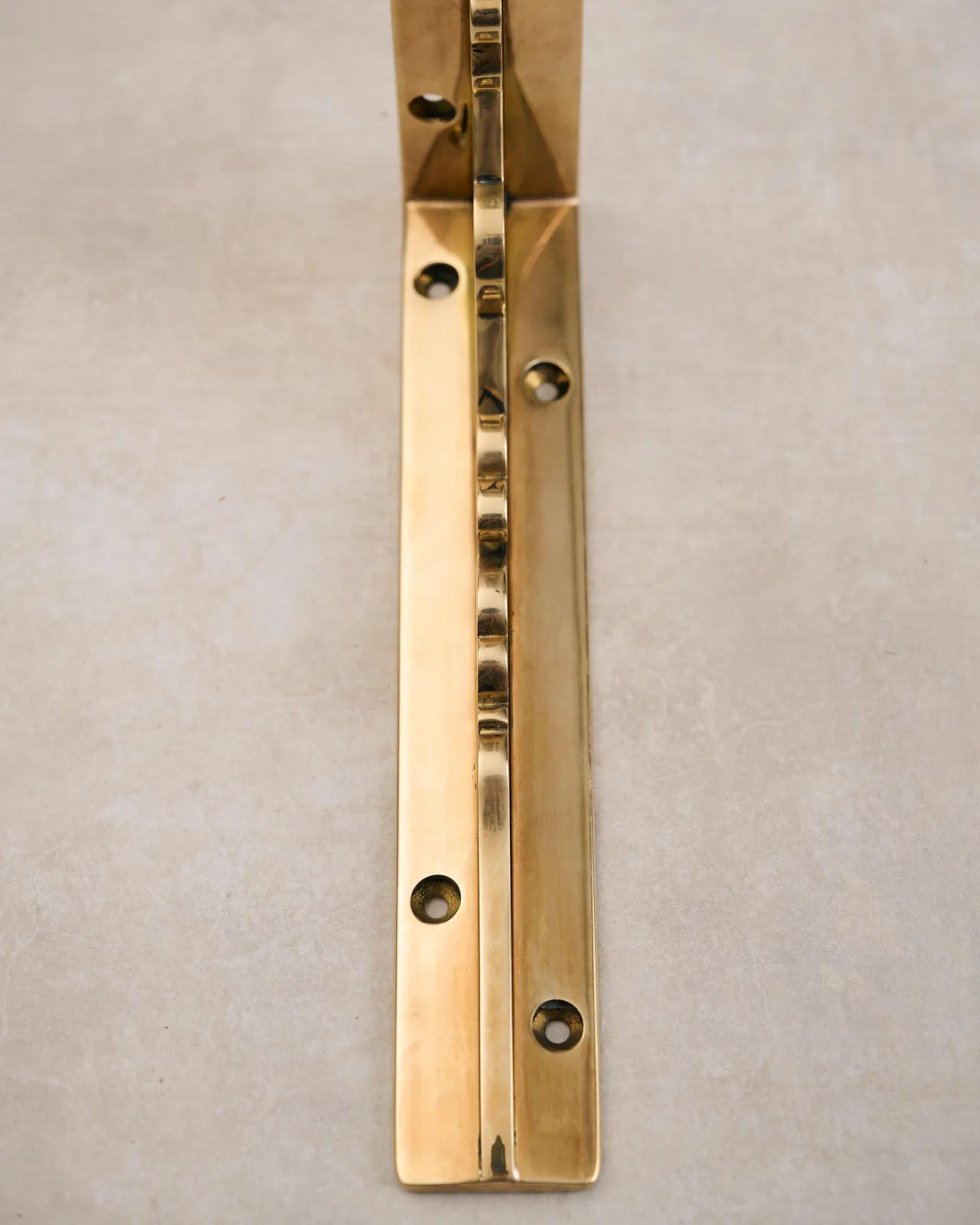 A close-up front profile view of a small Victorian-inspired ornate shelf bracket in a warm polished brass finish.