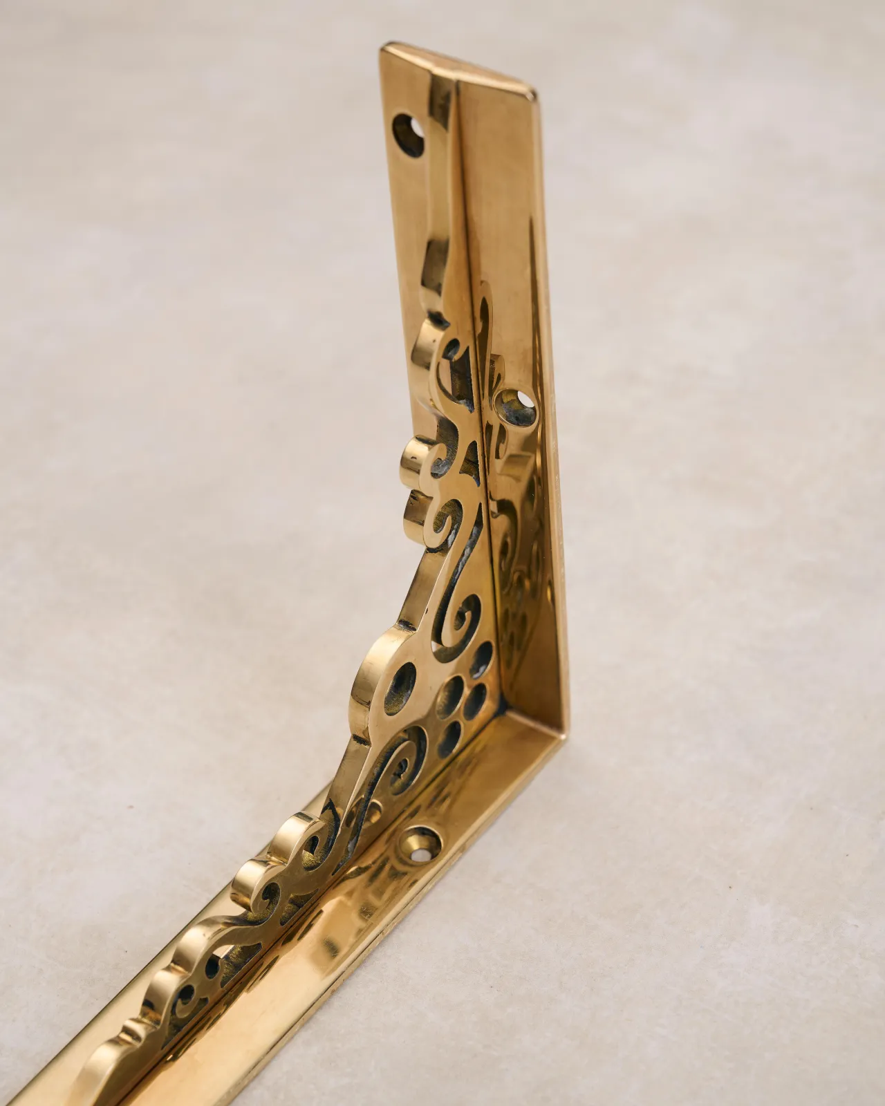 A close-up oblique view of a small Victorian-inspired ornate shelf bracket in a warm polished brass finish.