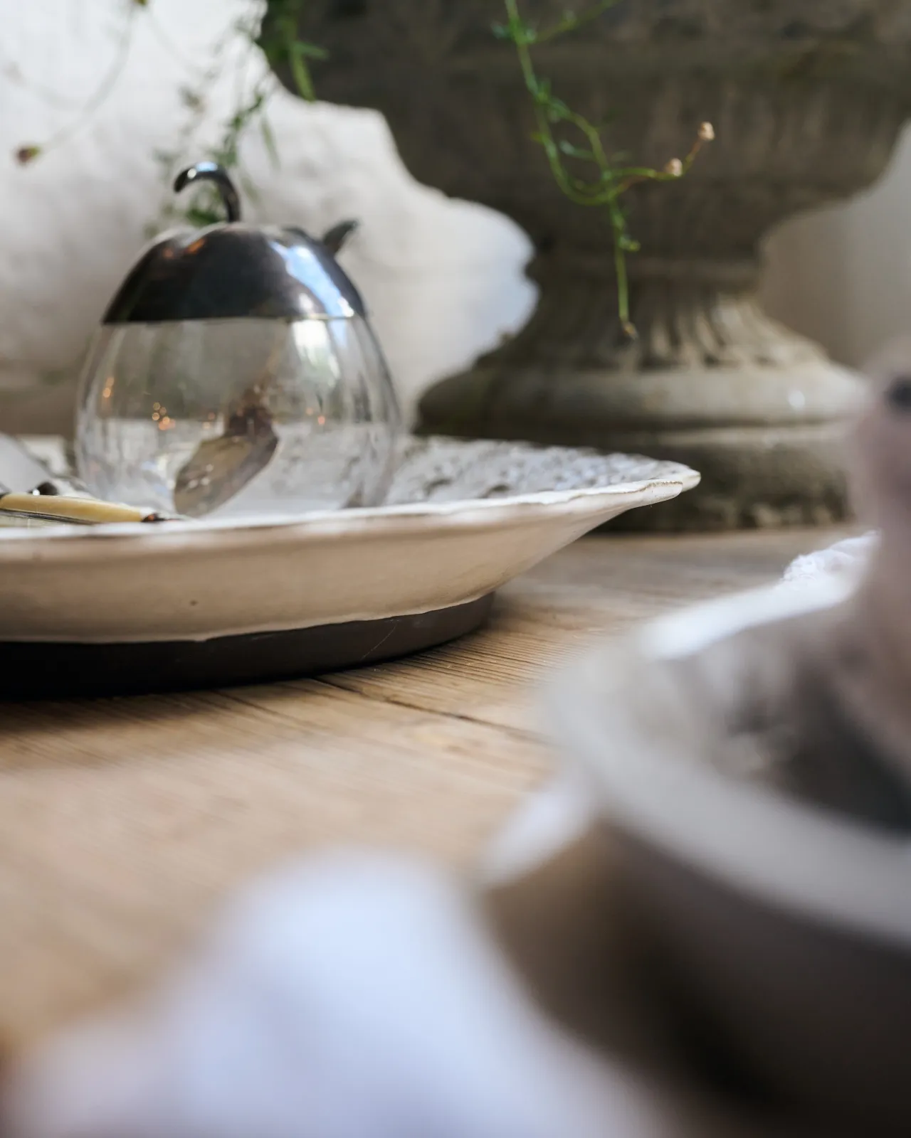 A profile view of a round handmade bohemian-style white ceramic platter on a vintage farmhouse table.