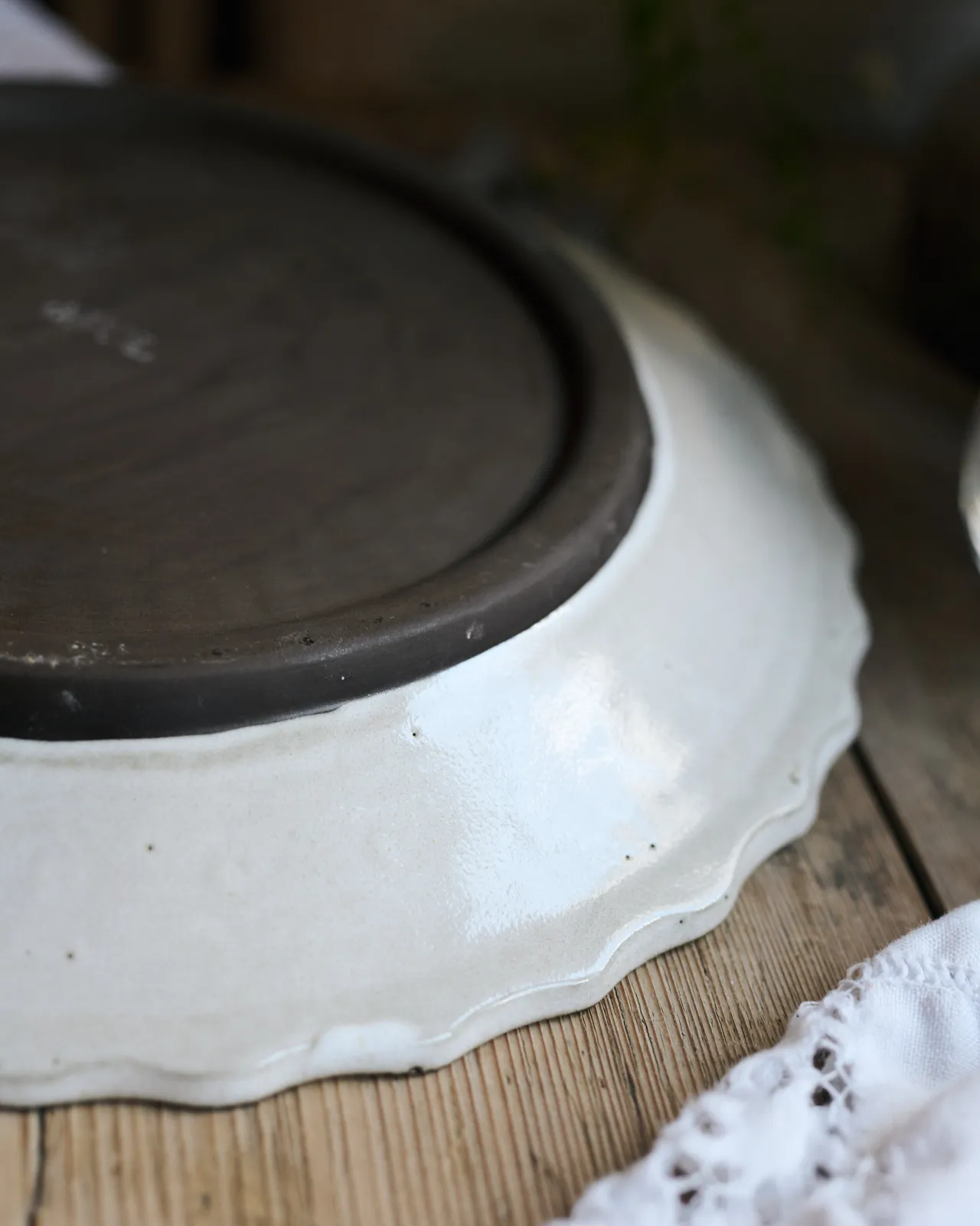 A close-up view of the underside of a white glazed rim and unglazed clay foot of a handmade bohemian-style ceramic platter.