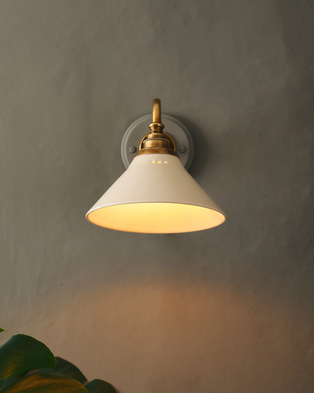 A front profile view of a small Victorian-inspired wall light with a swan neck brass arm and a cream glazed ceramic shade.