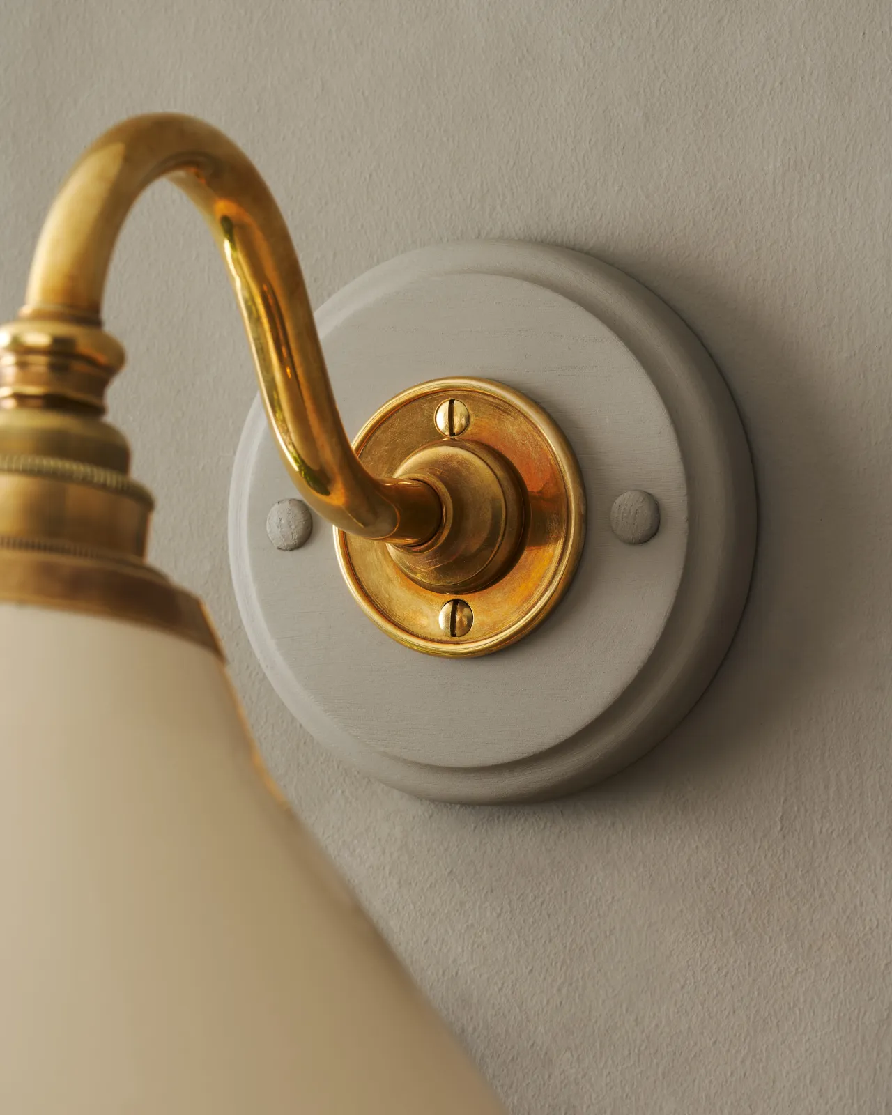 A close-up view of a swan neck brass arm fixed to a round oak pattress with a painted finish to match a grey wall.