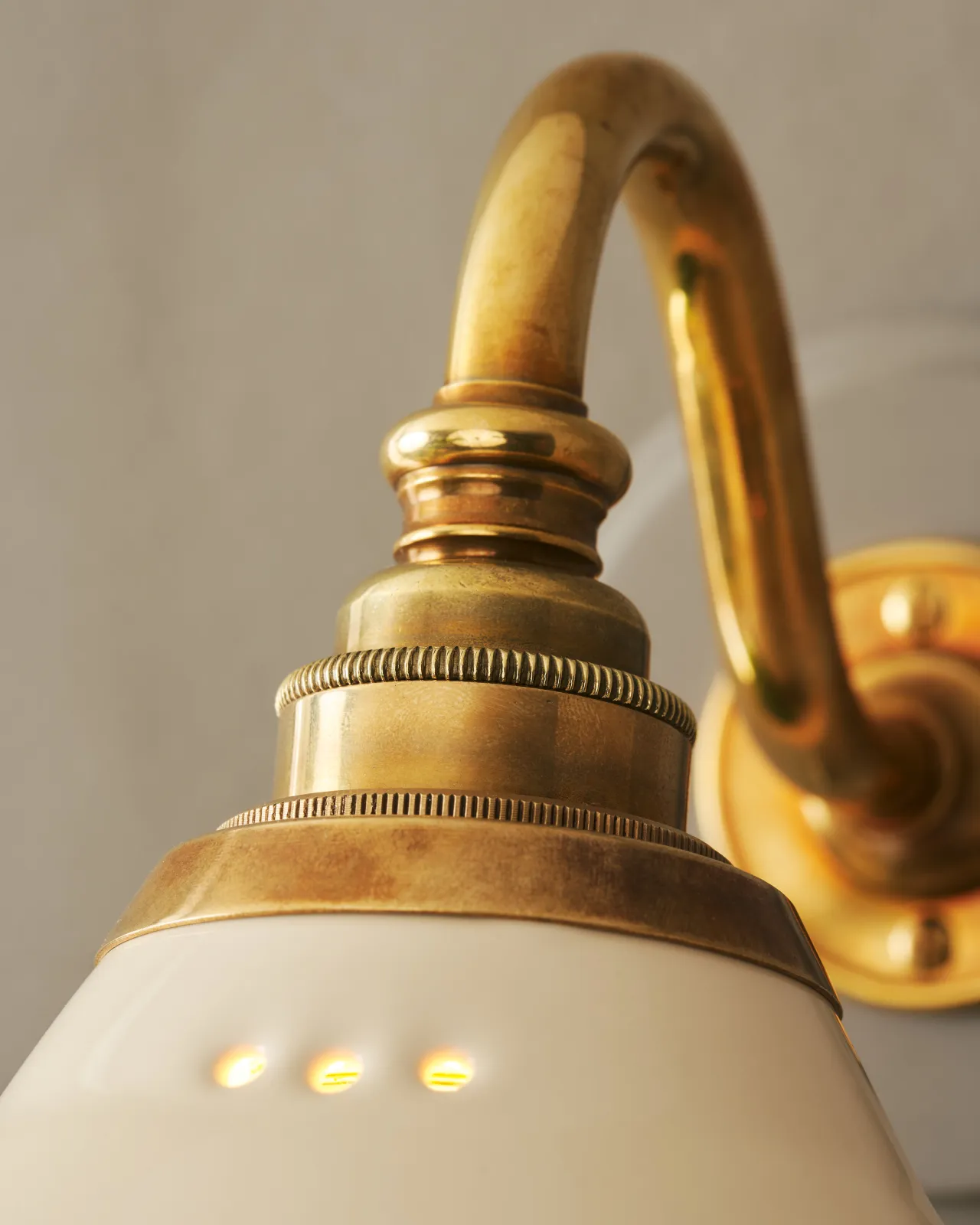 A close-up view of a swan neck brass arm and cuff, connected to a cream glazed ceramic light shade.