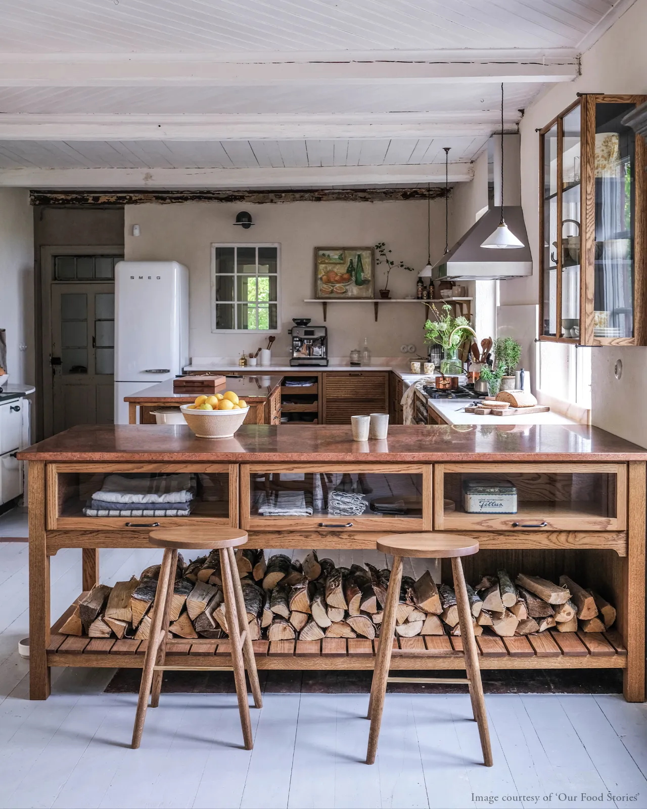 A straight-on view of a Scandinavian-style oak kitchen with an island peninsula and two simple oak bar stools with oval-shaped seats and brass footrails.