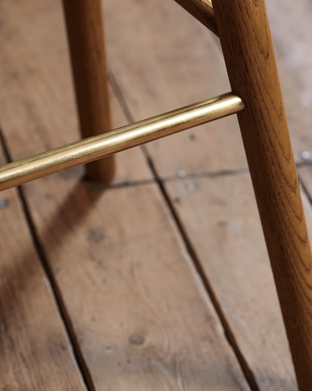 A close-up view of a brass footrail from an oak bar stool.