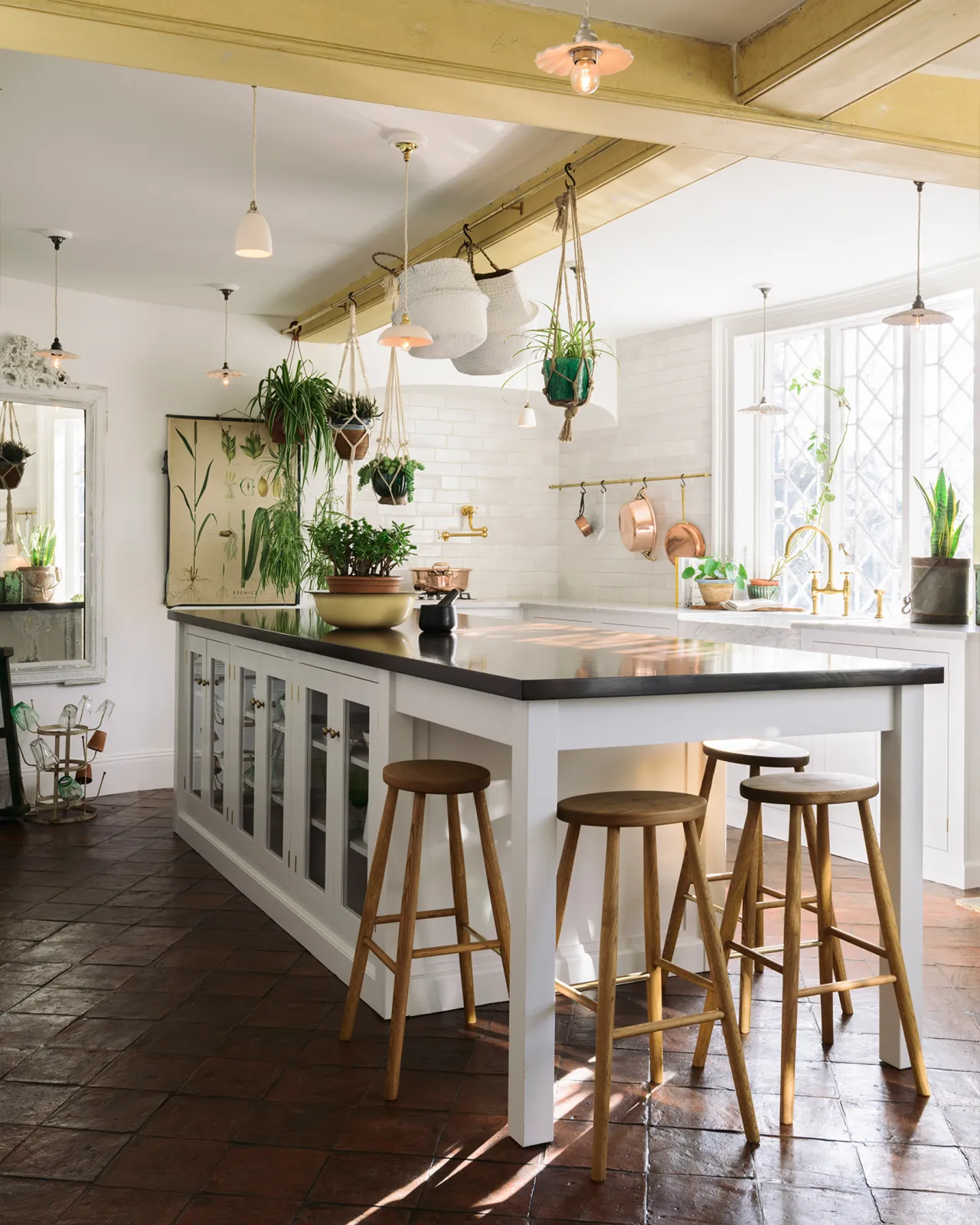 An oblique view of a Mediterranean-style classic kitchen with white painted cabinetry and an island with a dark hardwood worktop and four simple oak bar stools tucked into a breakfast bar end.