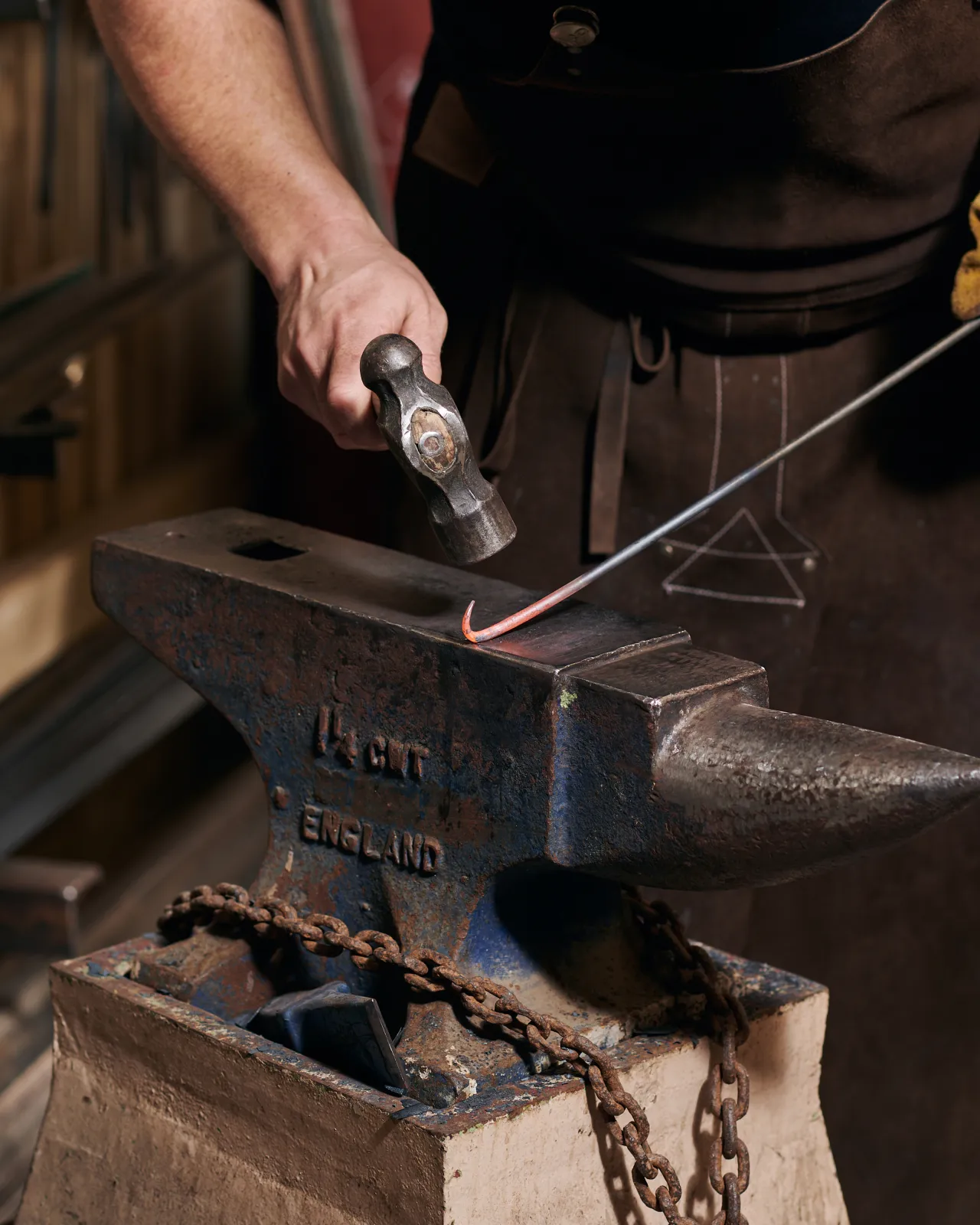 The red-hot end of an iron rod is being hammered into a simple curl on an anvil.