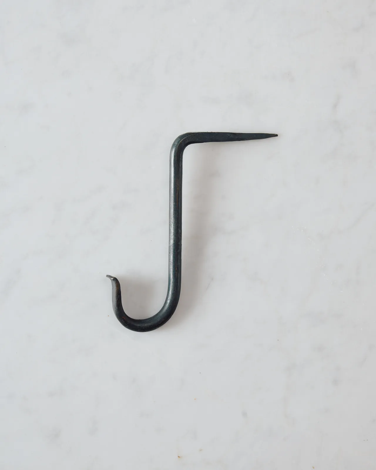 A side profile view of a large iron beam hook with a curled end.