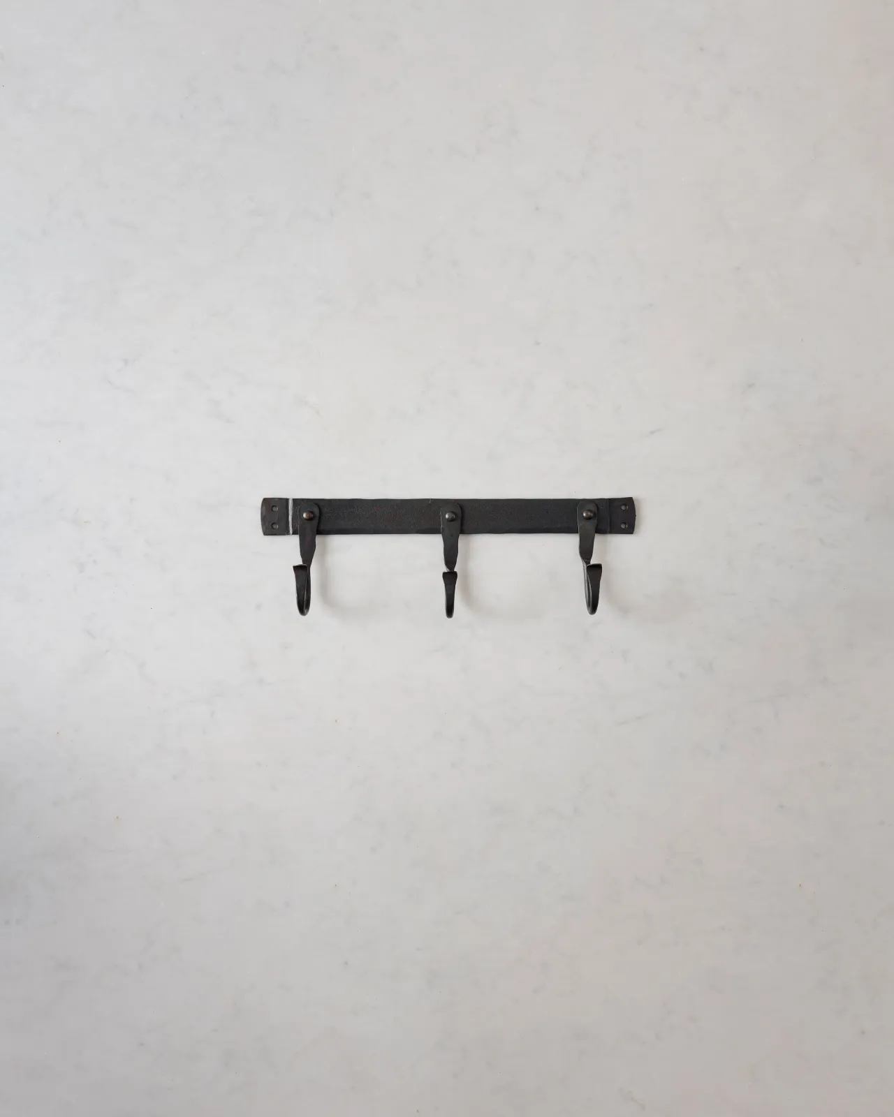 A small iron hook rack with three hooks spread evenly across the length.