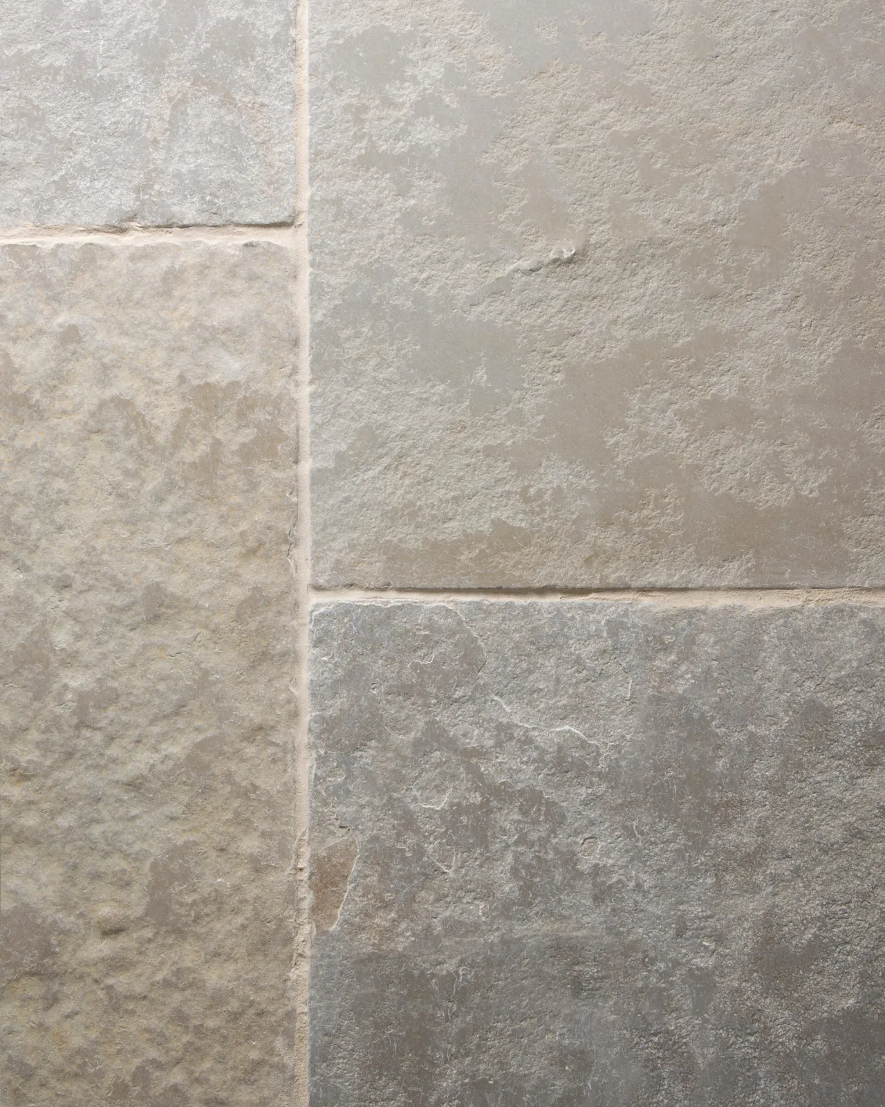 A close-up overhead view of Jaipur Brushed Limestone flooring, showing the textured surface and subtle variation in colour in each tile. Two loose tiles are stacked in the top left corner.