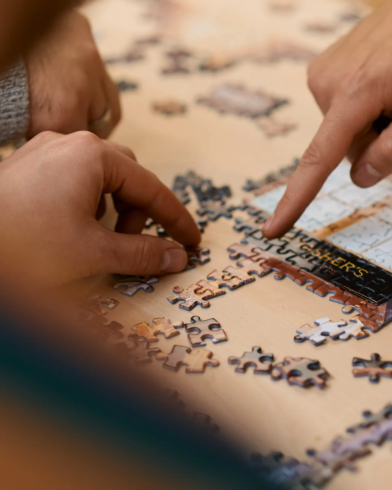 A close-up view of a half-completed jigsaw puzzle with hands pointing at pieces.