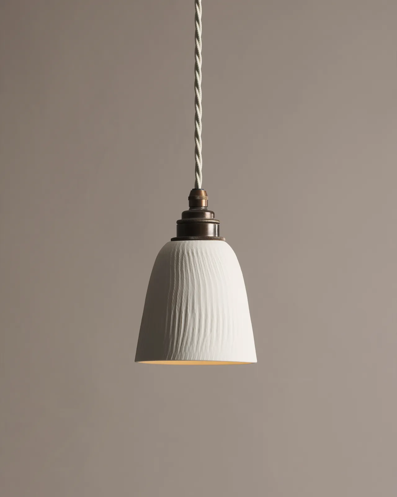 A large chattered beaker porcelain pendant light with an unglazed finish, an aged brass E27 lampholder and a white twisted fabric flex cord.