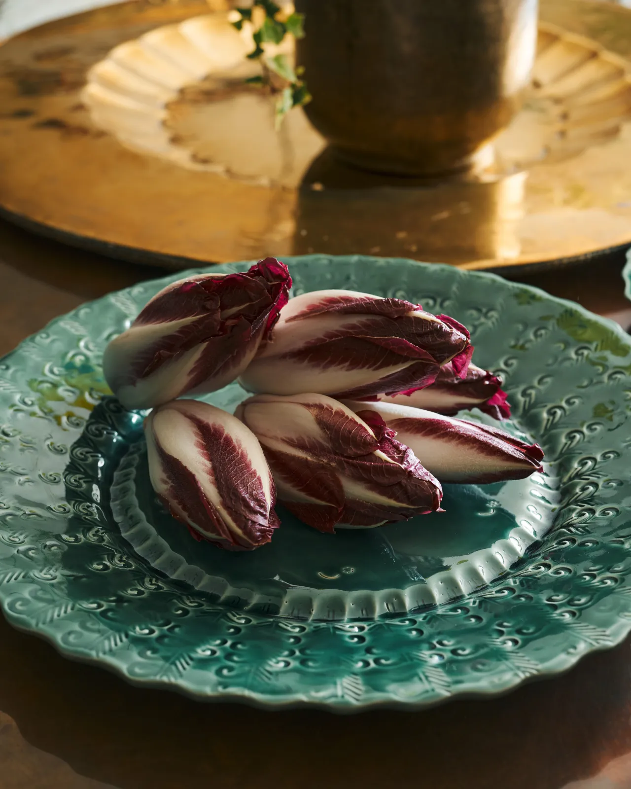 Red chicory on a large handmade bohemian-style green ceramic platter with a scalloped rim and delicate impressions and surface patterns.
