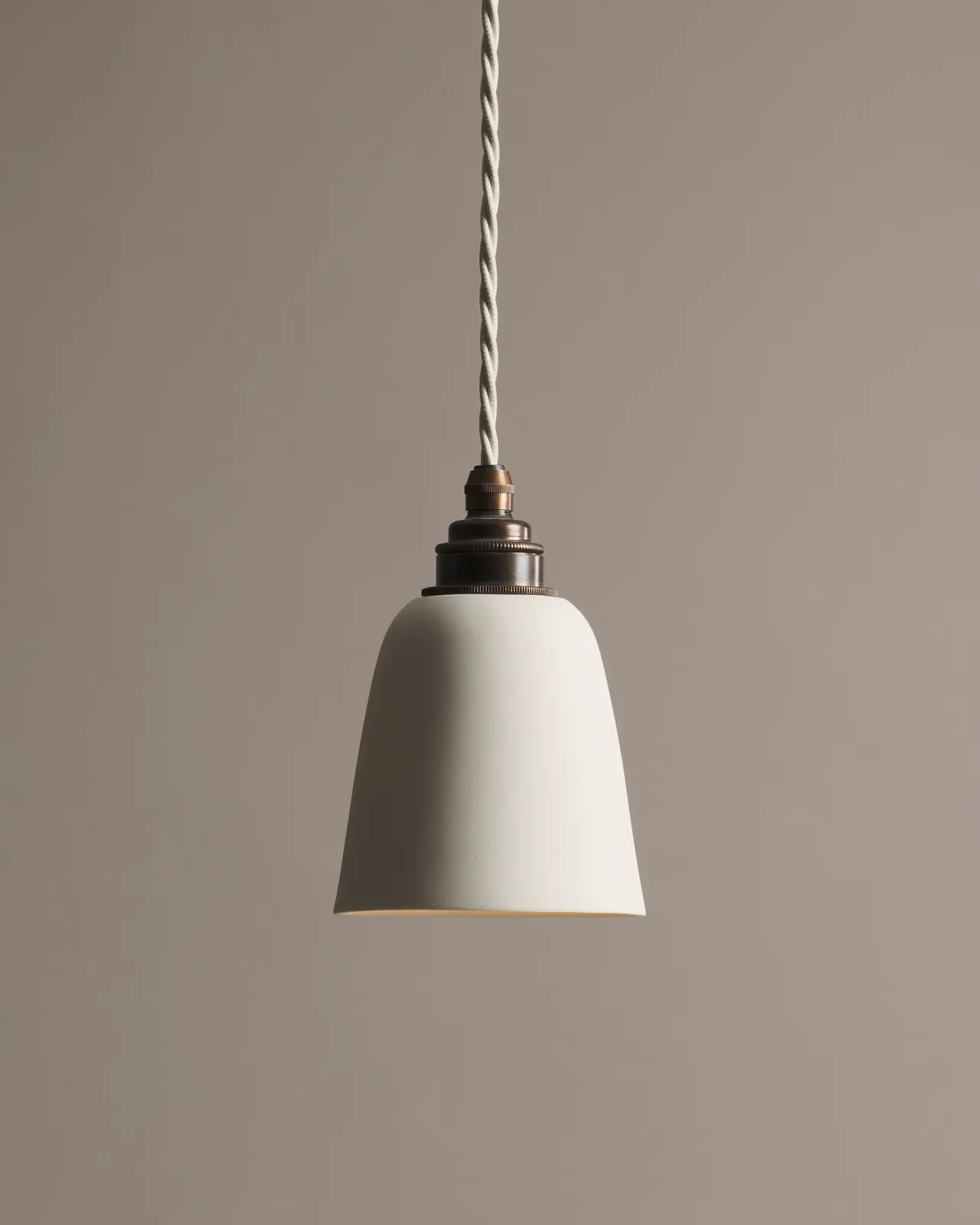 A large plain beaker porcelain pendant light with an unglazed finish, an aged brass E27 lampholder and a white twisted fabric flex cord.