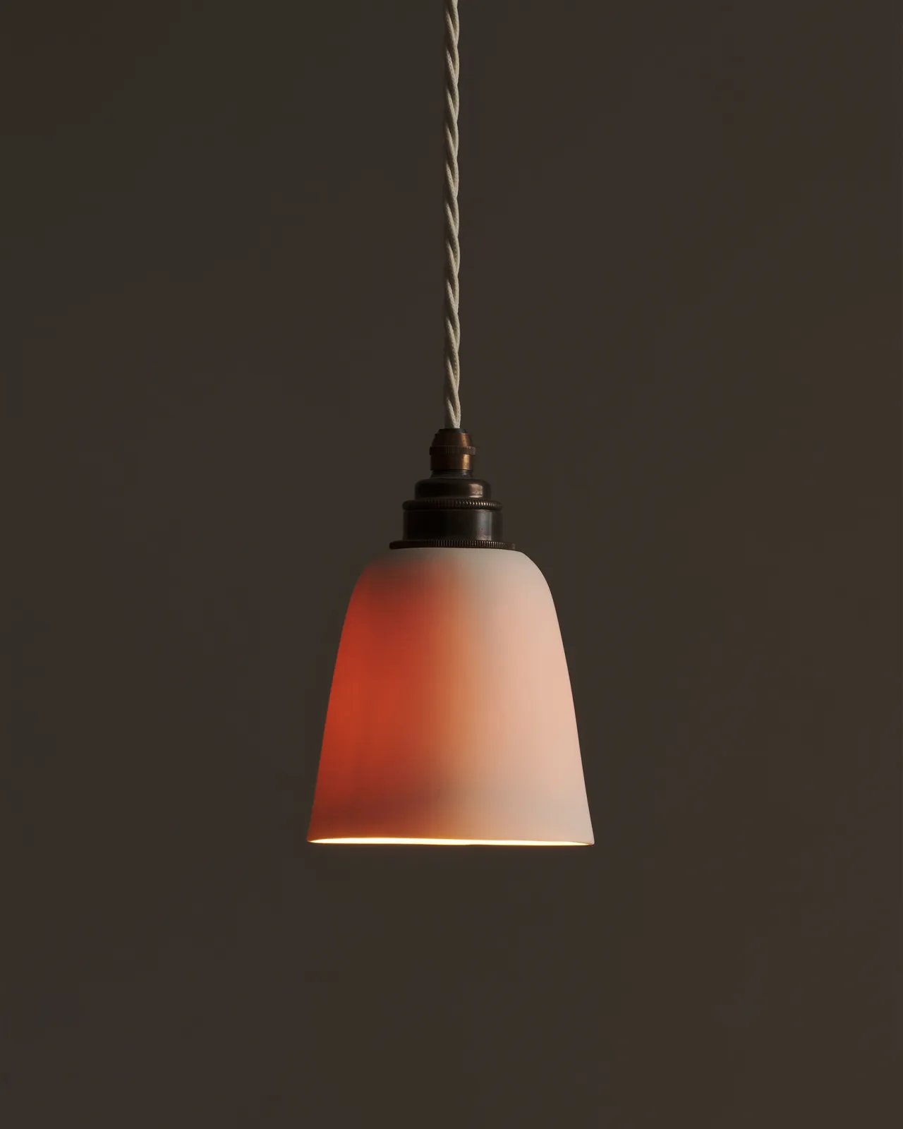 A large plain beaker porcelain pendant with the light on, showing the warm red glow of the translucent surface.