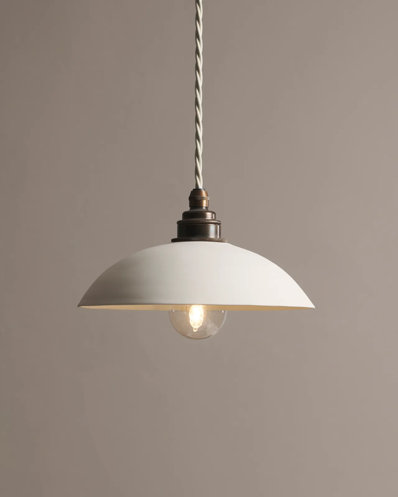 A large plain skullcap porcelain pendant light with an unglazed finish, an aged brass E27 lampholder and a white twisted fabric flex cord.