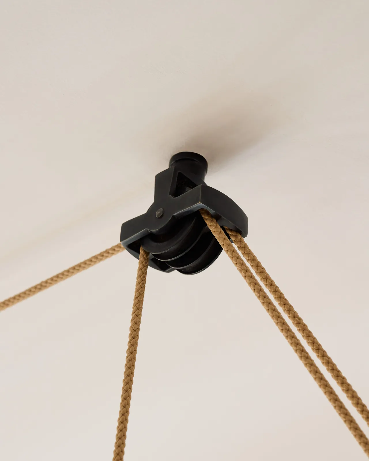 A close-up view of a black brass wheel pulley fixed to a white ceiling.