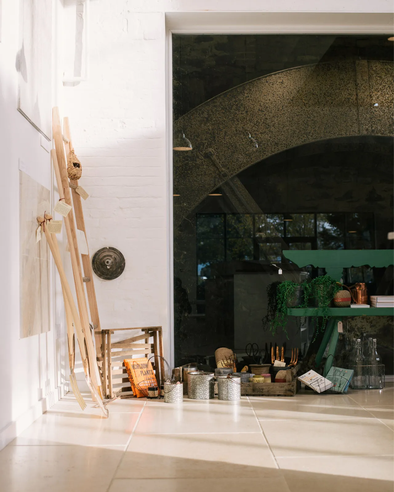 A straight-on shot looking towards the back of deVOL's flooring showroom, with a beautiful, huge old mill wheel behind a pane of glass, white painted brick walls and smooth, creamy Light Jerusalem Limestone flooring.