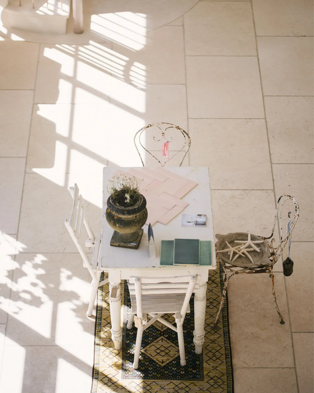 Looking down towards a little writing desk and four antique chairs in deVOL's flooring showroom. Light streams through the huge glazed wall, leaving pools of light and shadows on the beautiful Light Jerusalem Limestone flooring.