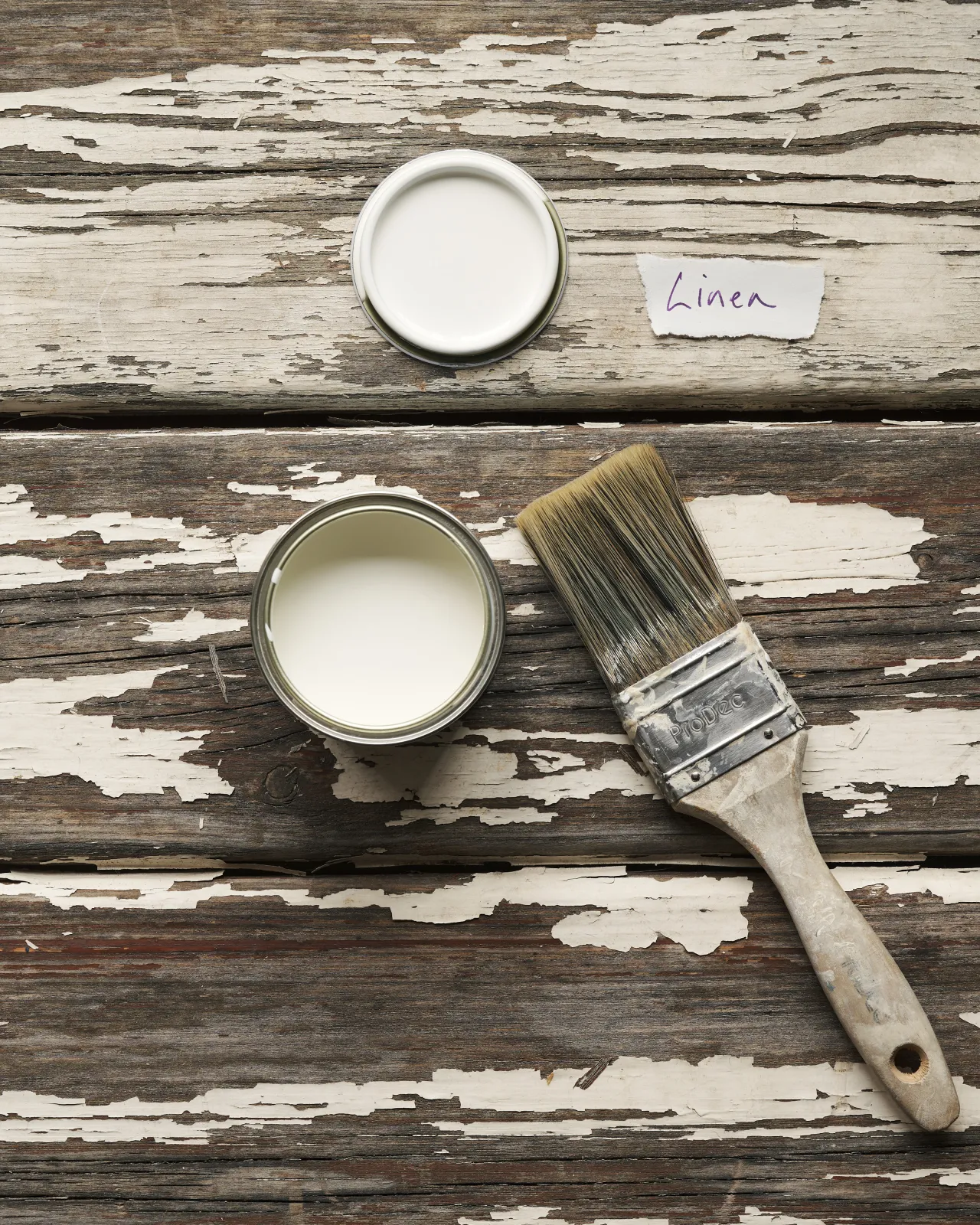 An overhead view of an open paint pot and a worn brush on a rustic tabletop. The light cream colour inside is labelled 'Linen'.