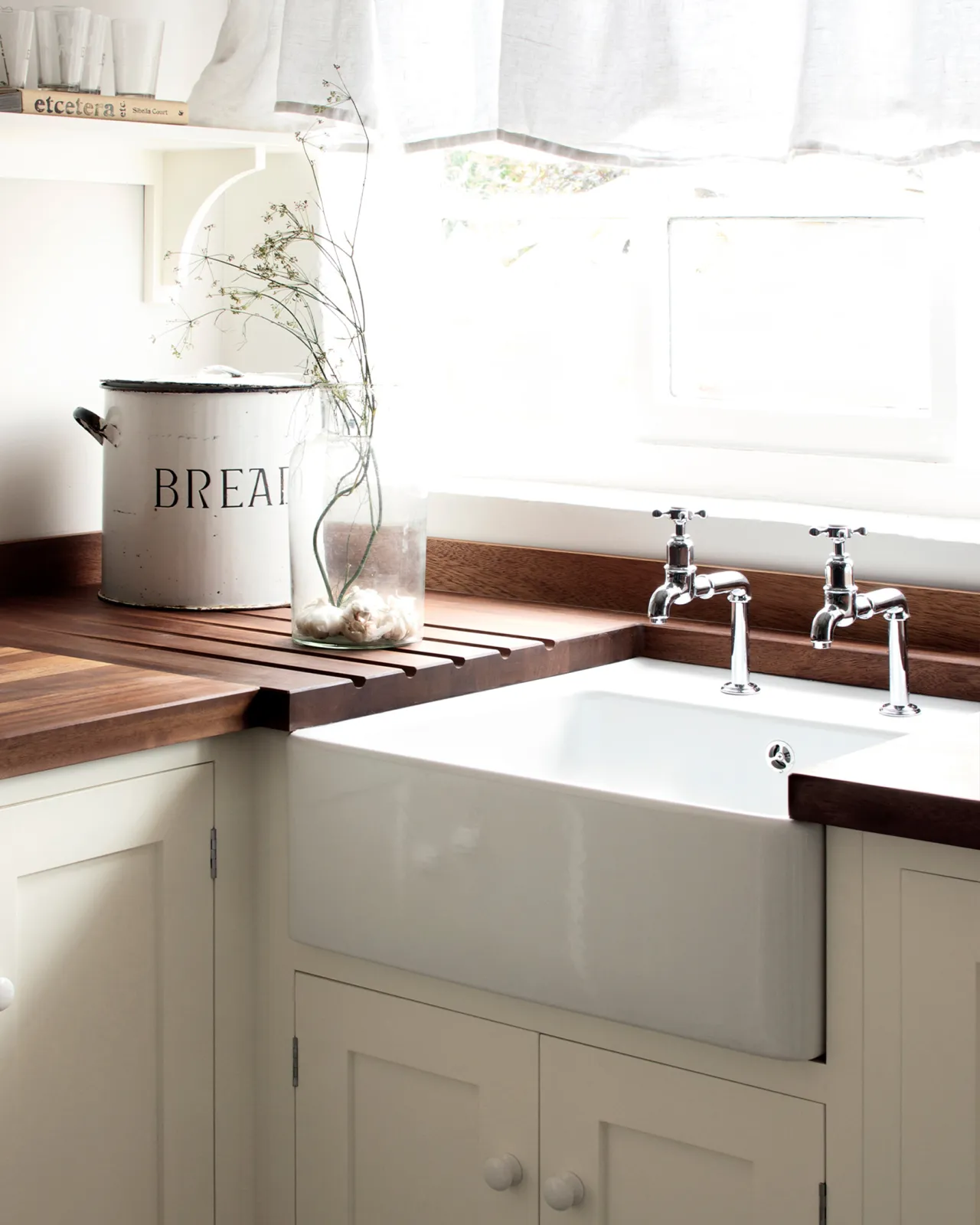 A pair of traditional-style chrome bibcock taps with crosshead handles in a small cottage-style kitchen with a white ceramic Belfast sink and rich stave hardwood worktops.