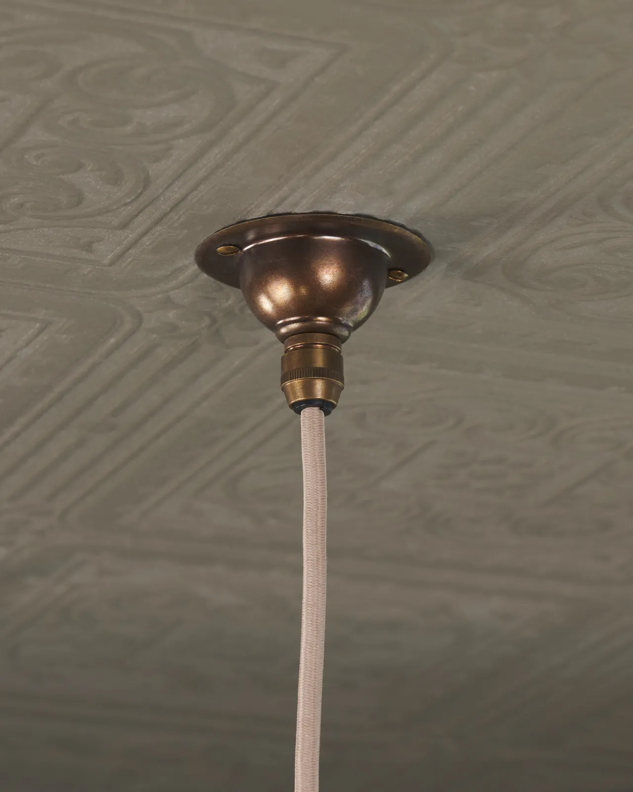 A small aged brass ceiling rose with a beige fabric flex cord.