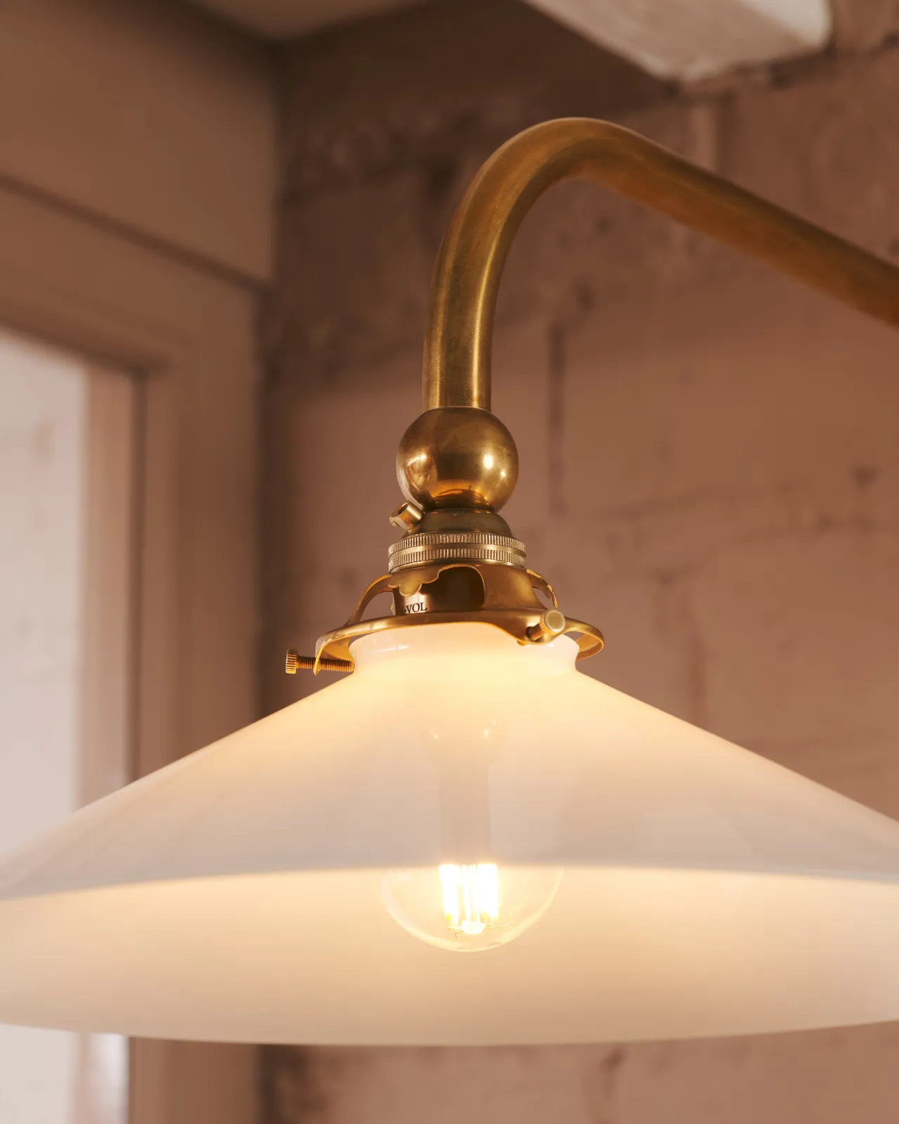 A close-up view of a decorative brass gallery and light fitting attached to a milk glass light shade.
