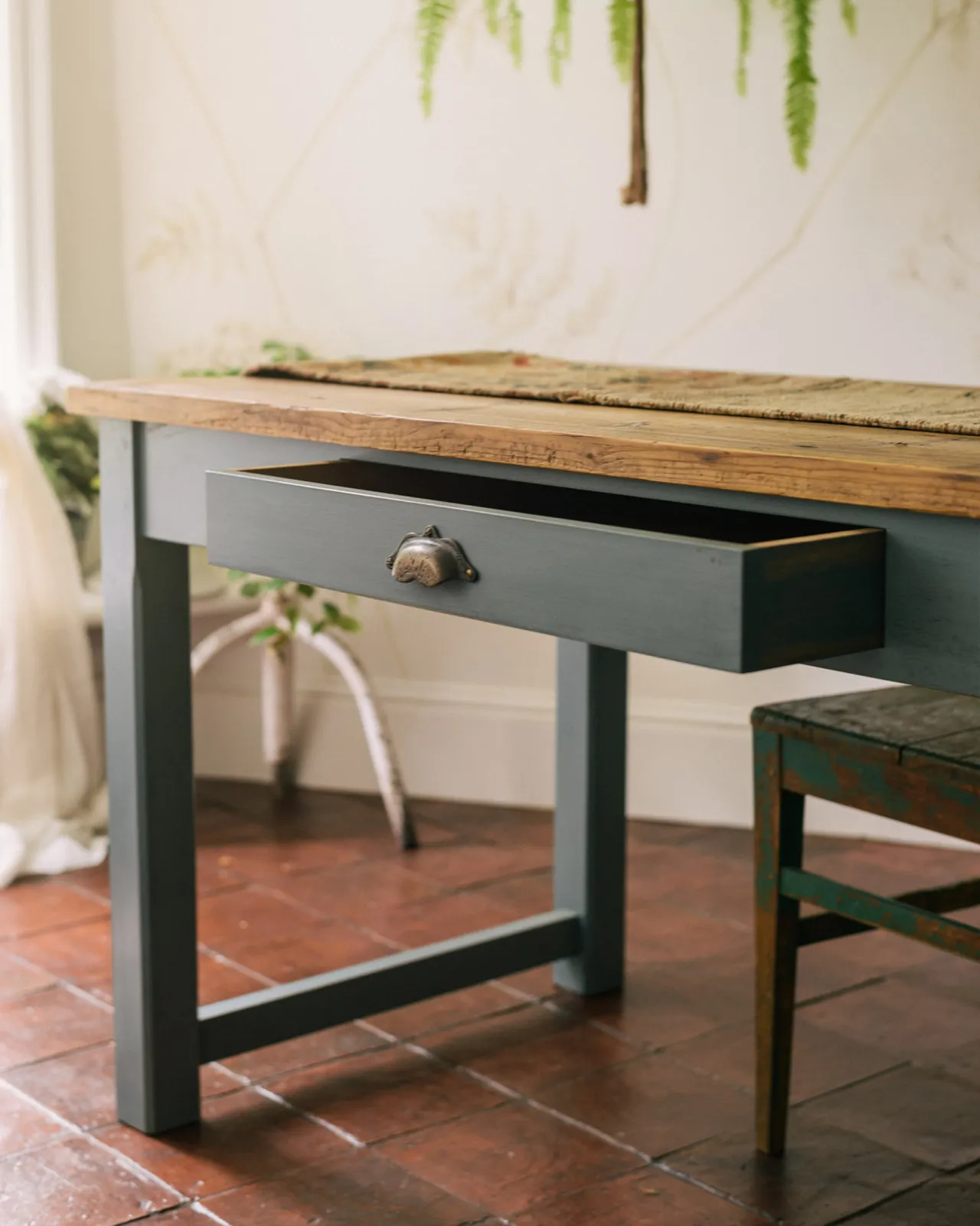 An oblique view of a shallow drawer with a bohemian-style brass handle from a banquet-style dining table.