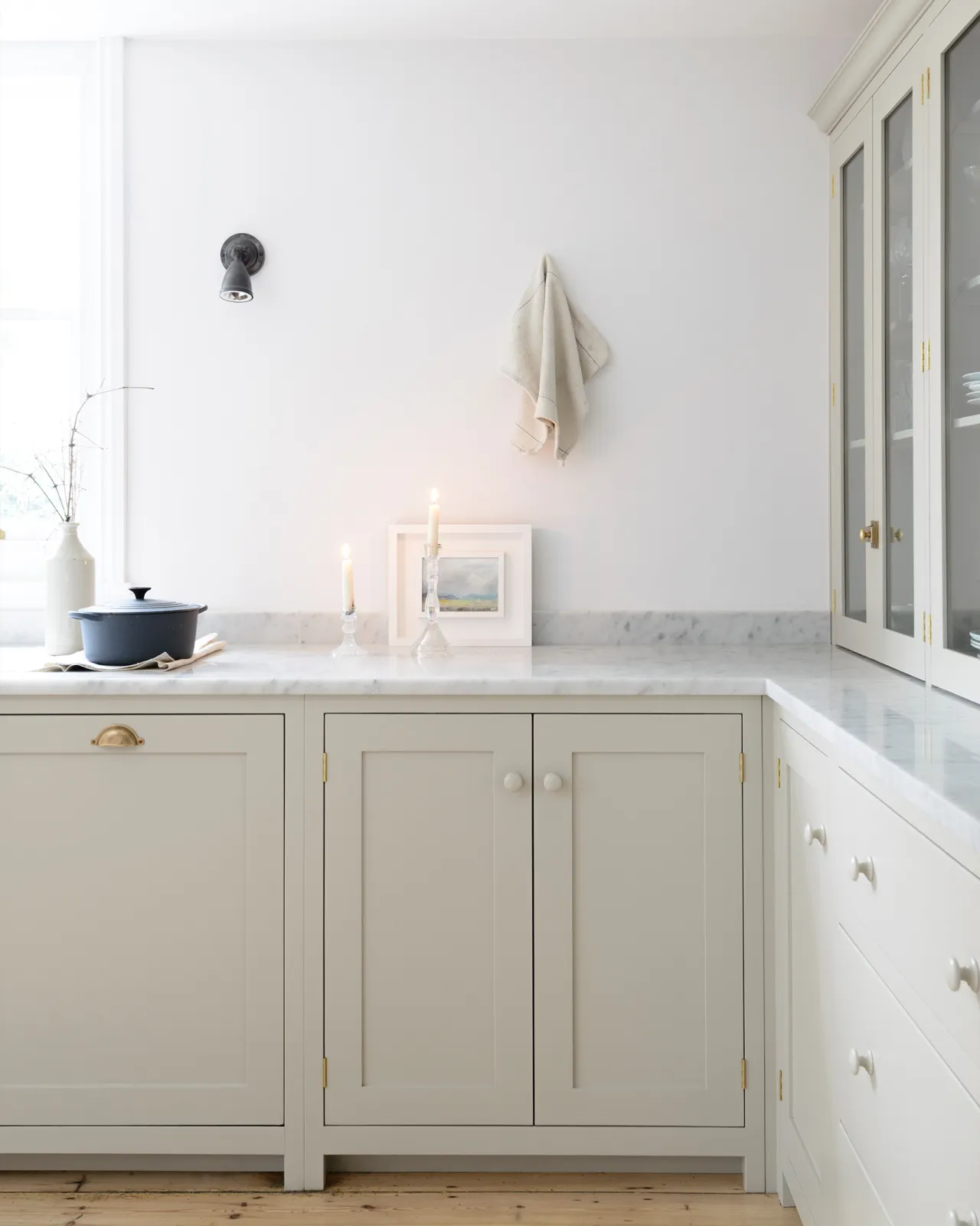 A simple Shaker-style kitchen corner with creamy mushroom coloured cupboards, white walls, a Carrara marble worktop and a lit candle.