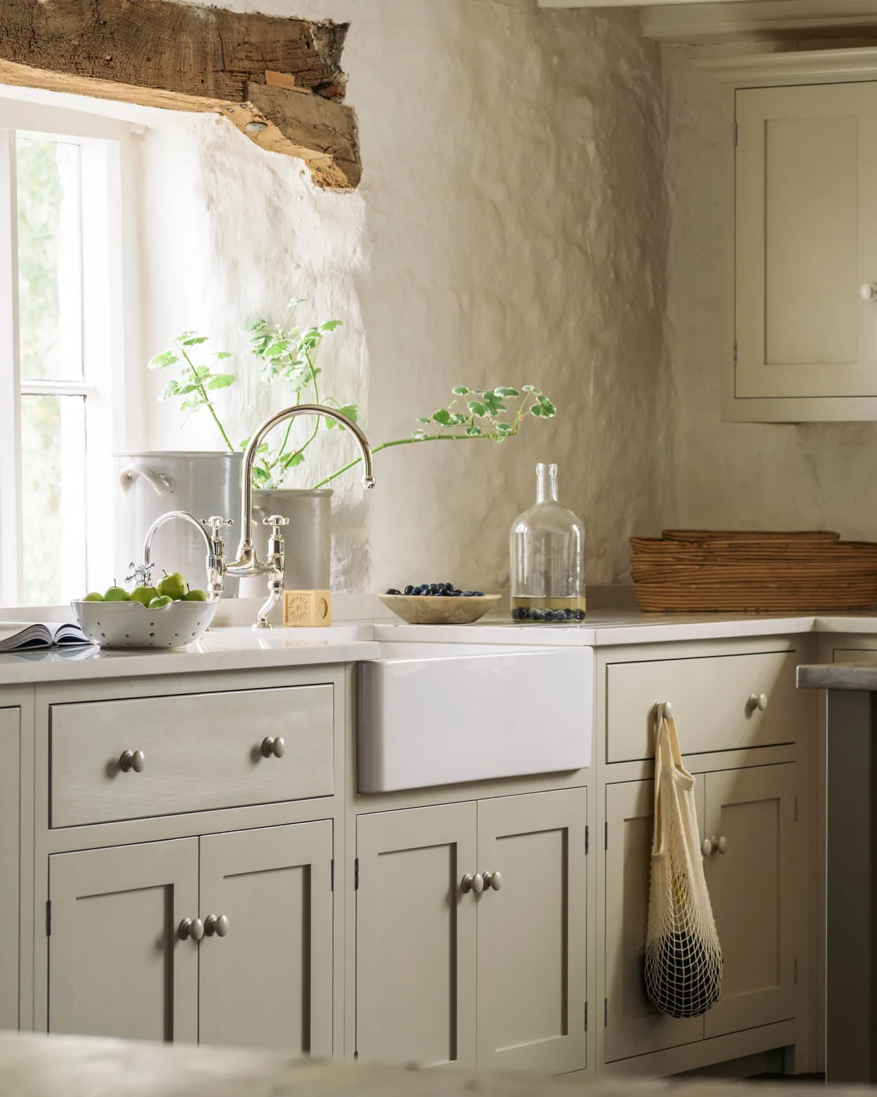 An oblique view of a Shaker-style kitchen sink cupboard, painted in a creamy mushroom colour and paired with chrome taps and a white ceramic Belfast sink.