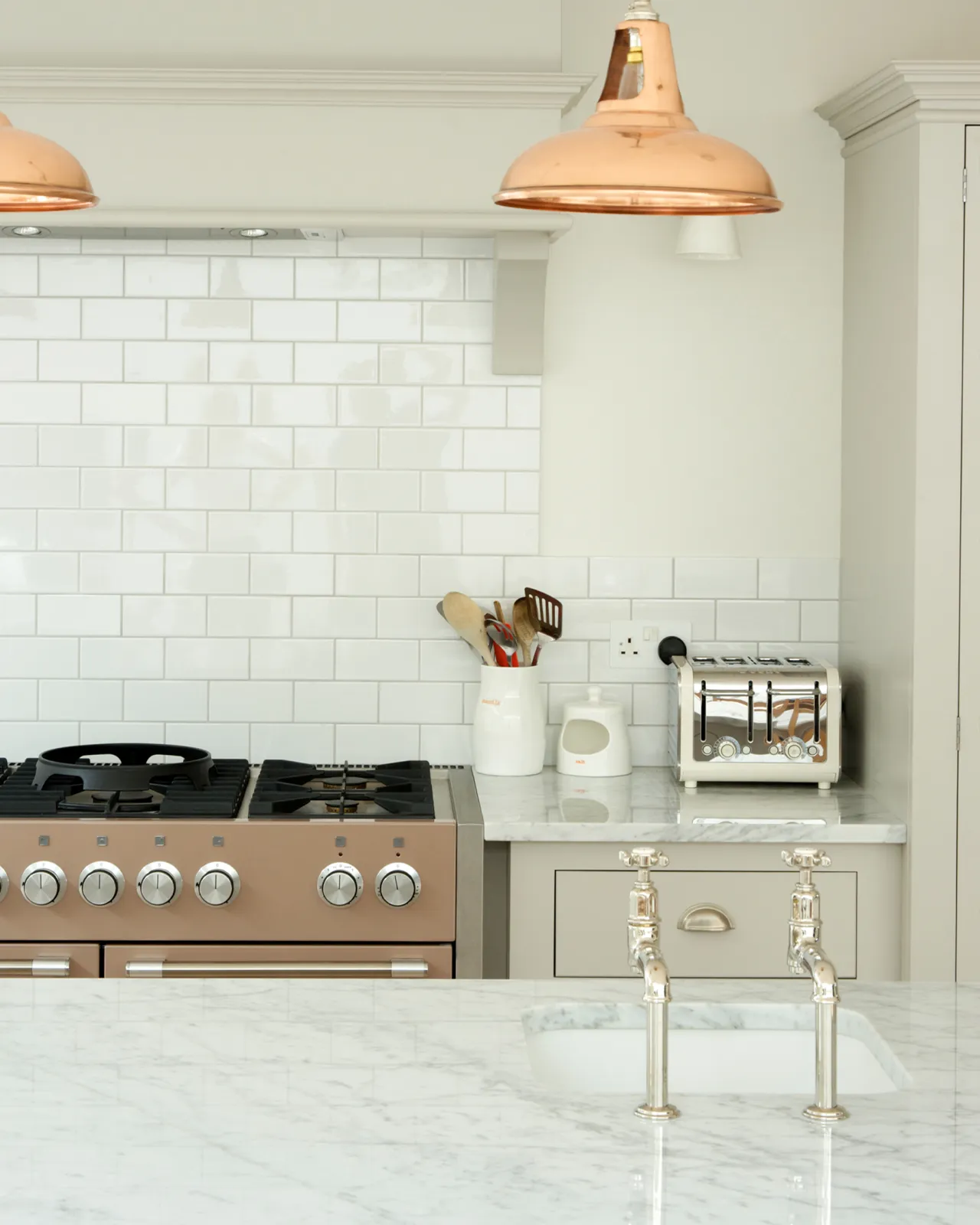 A straight-on view of a pair of traditional-style nickel bibcock taps with crosshead handles on a polished Carrara marble worktop.