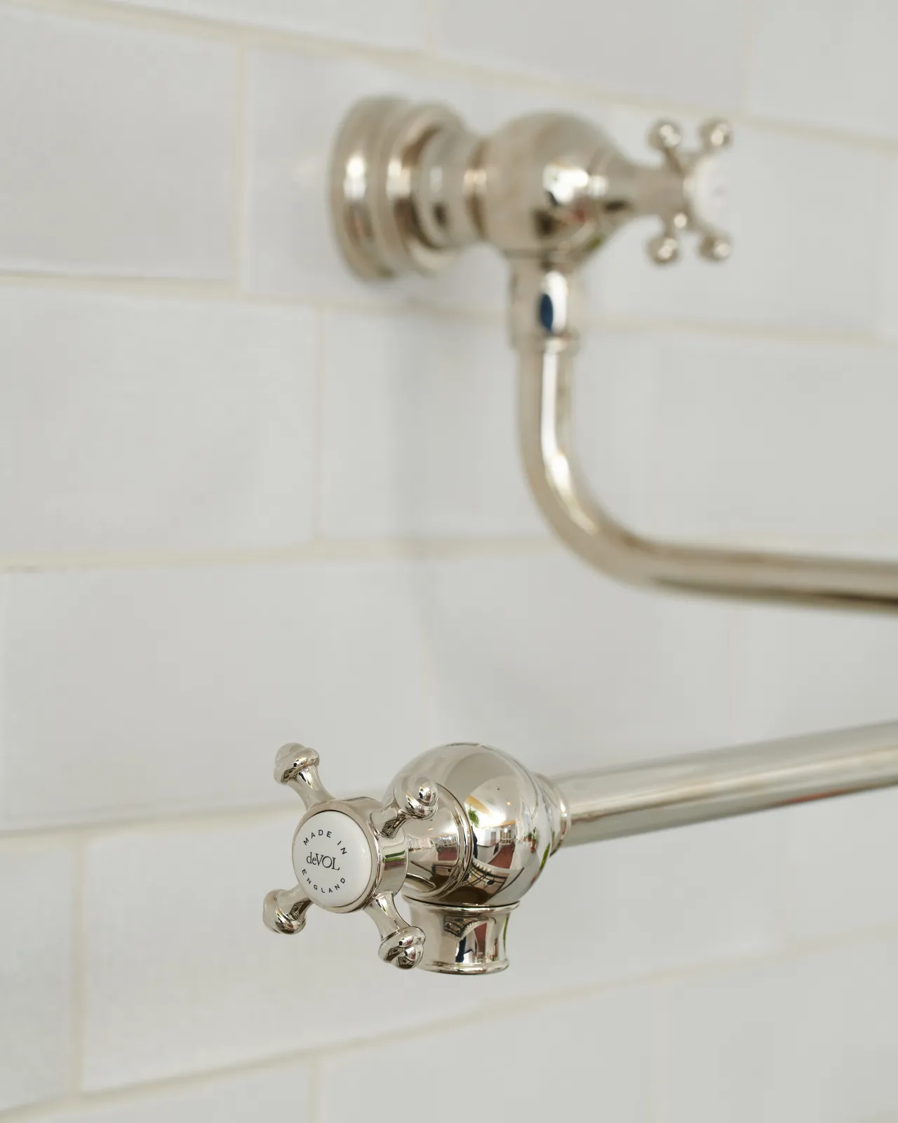 An oblique view of a traditional-style nickel pot filler tap with crosshead handles fitted to a wall of white metro tiles.