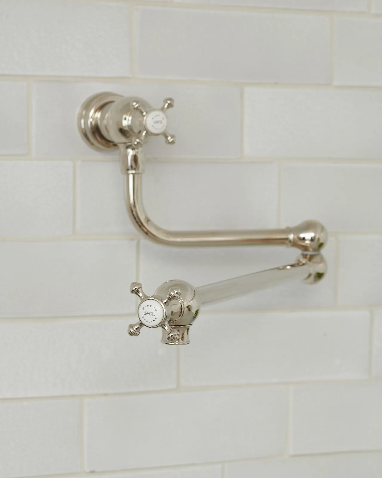 An oblique view of a traditional-style nickel pot filler tap with crosshead handles fitted to a wall of white metro tiles.