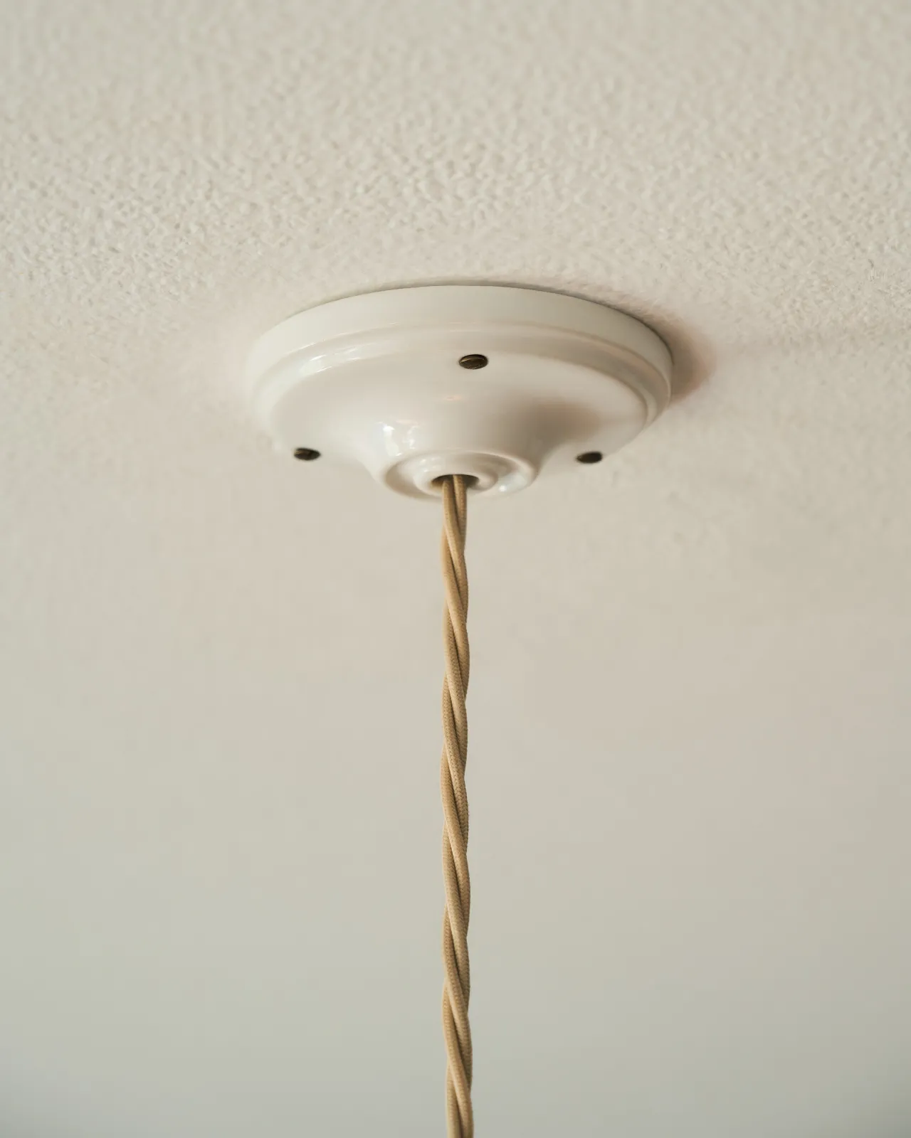 A white ceramic ceiling rose with cream twisted fabric flex cord.