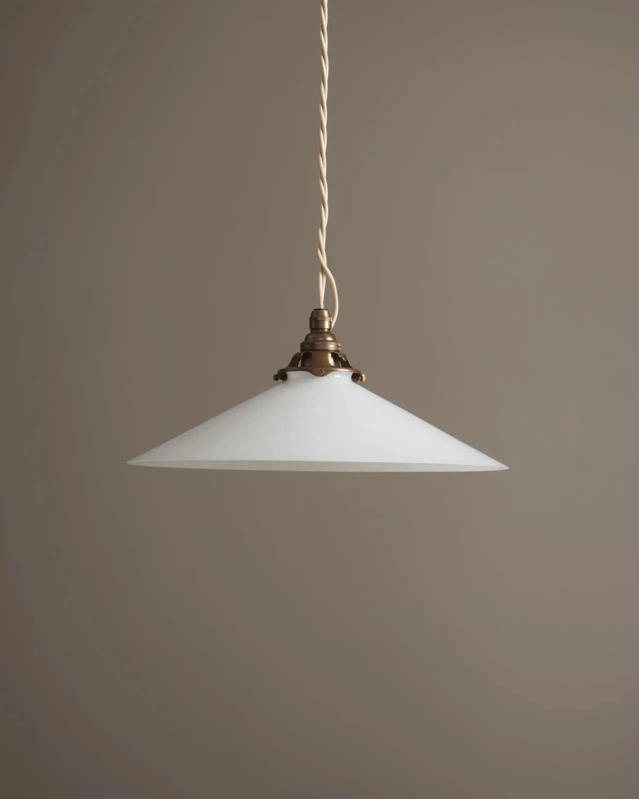 A classic pendant light with a milk glass light shade, an aged brass E27 lampholder with a decorative gallery and cream twisted fabric flex cord. The light is off.