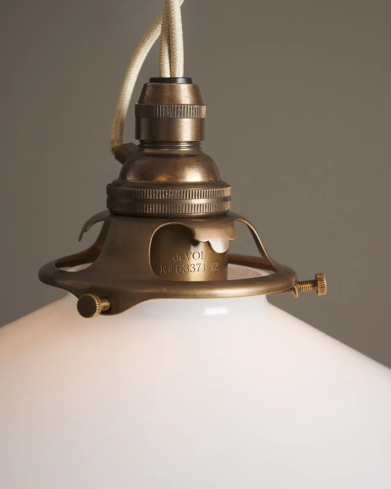 A close-up view of an aged brass E27 lampholder and a decorative brass gallery connected to the lip of a milk glass light shade.
