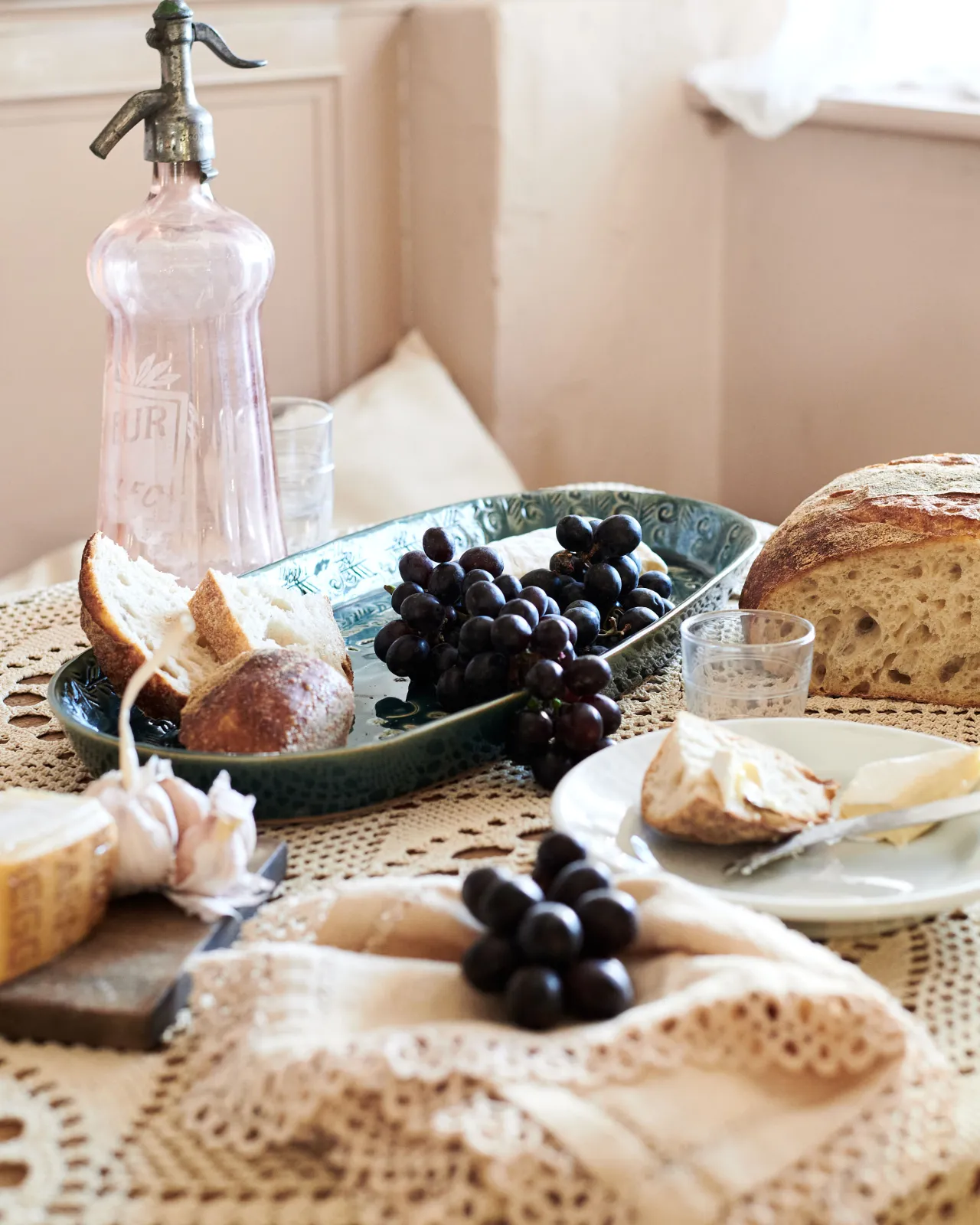 An oval-shaped handmade bohemian-style blue ceramic platter, with black grapes, cheeses and homemade bread.