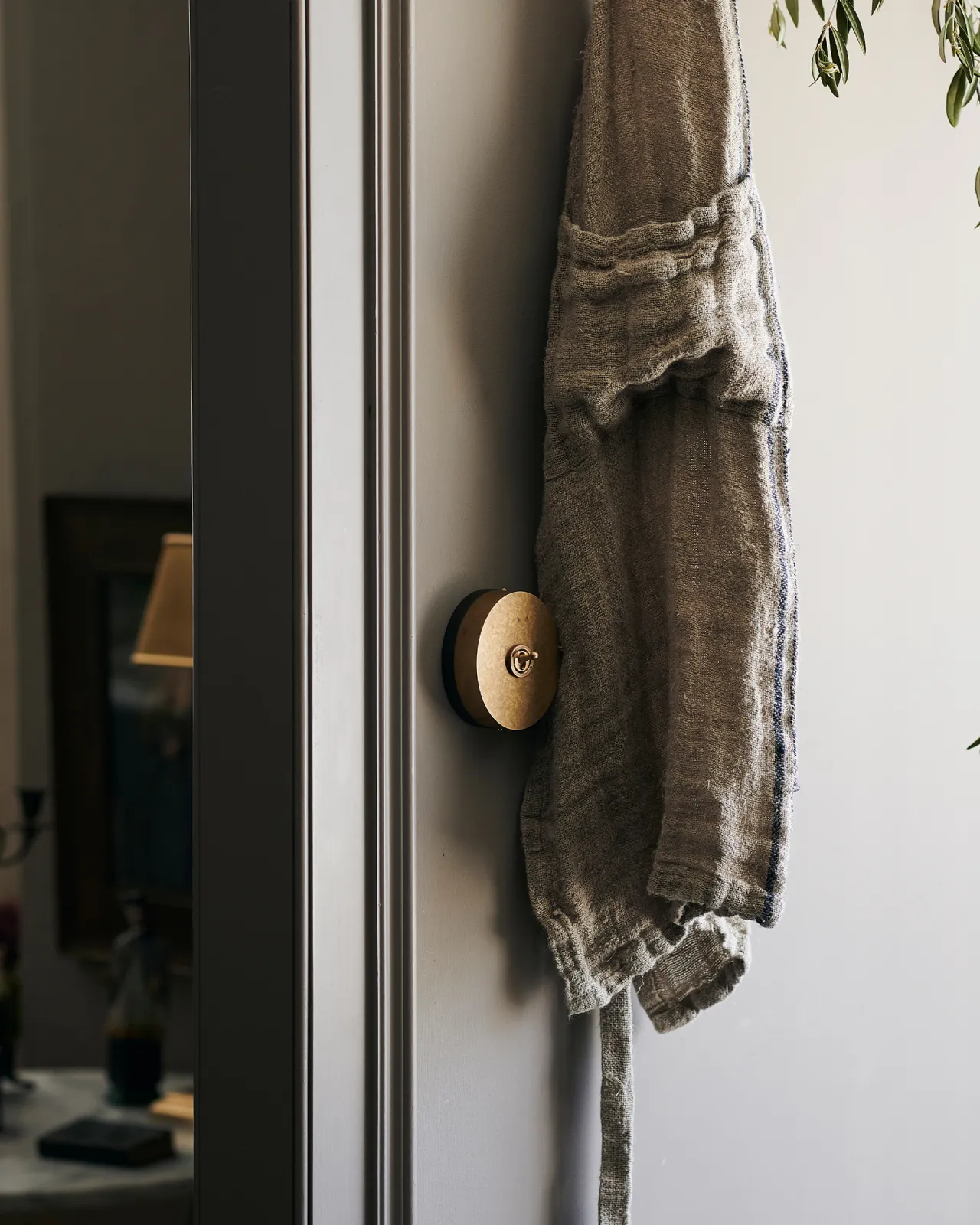A 1 gang oval-shaped toggle switch in aged brass on a grey wall, hiding behind a vintage linen apron.