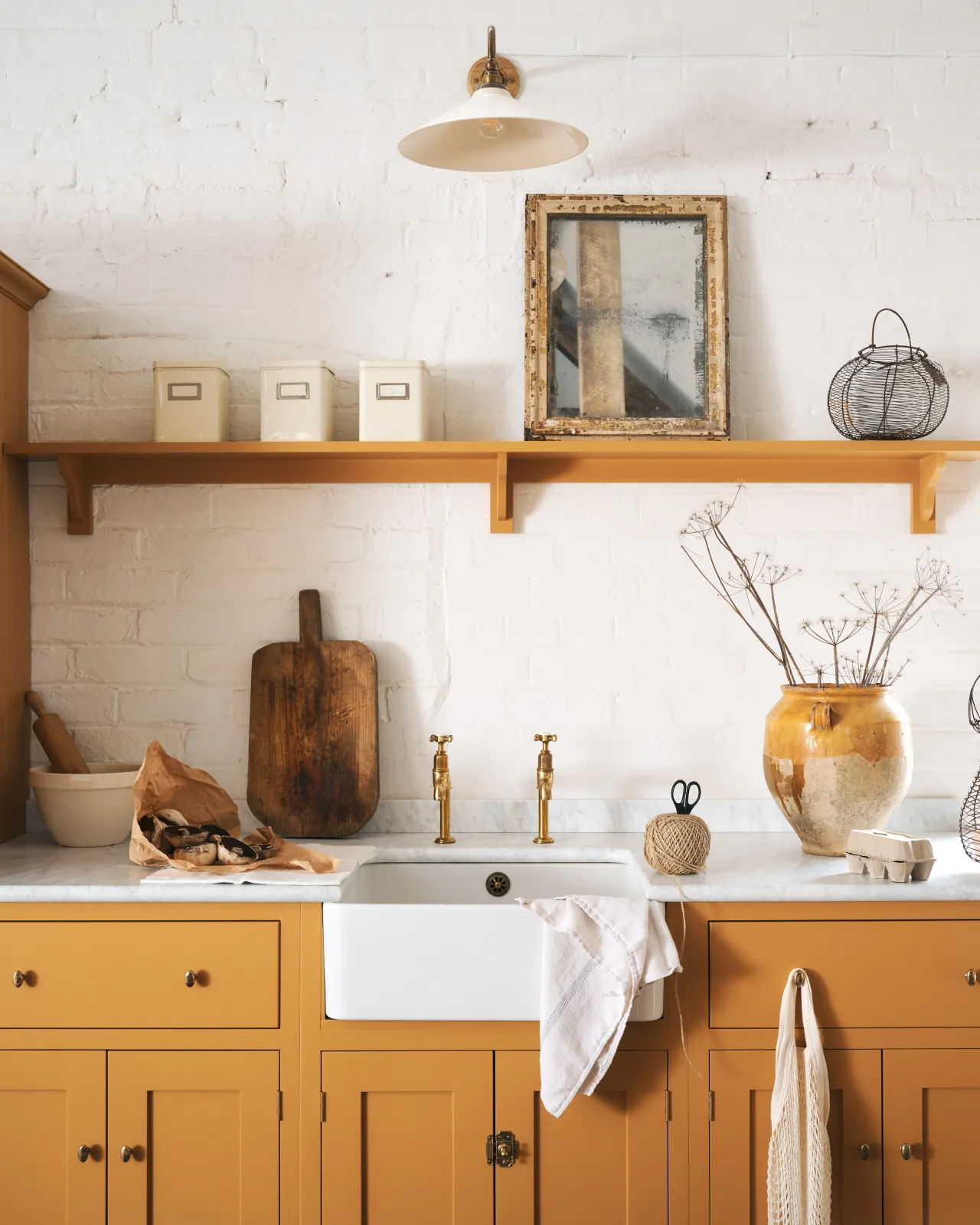 A straight-on view of a yellow painted Shaker-style kitchen sink cupboard with small oval-shaped knobs in a warm burnished brass finish.