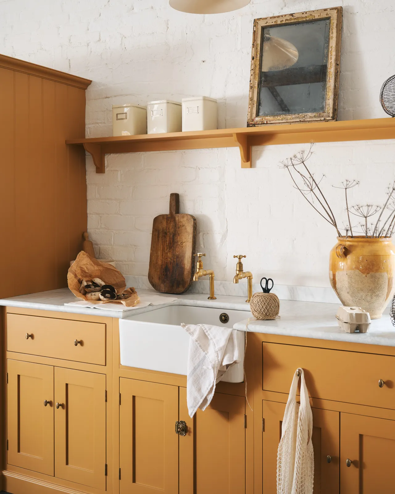 An oblique view of a yellow painted Shaker-style kitchen sink cupboard with small oval-shaped knobs in a warm burnished brass finish.