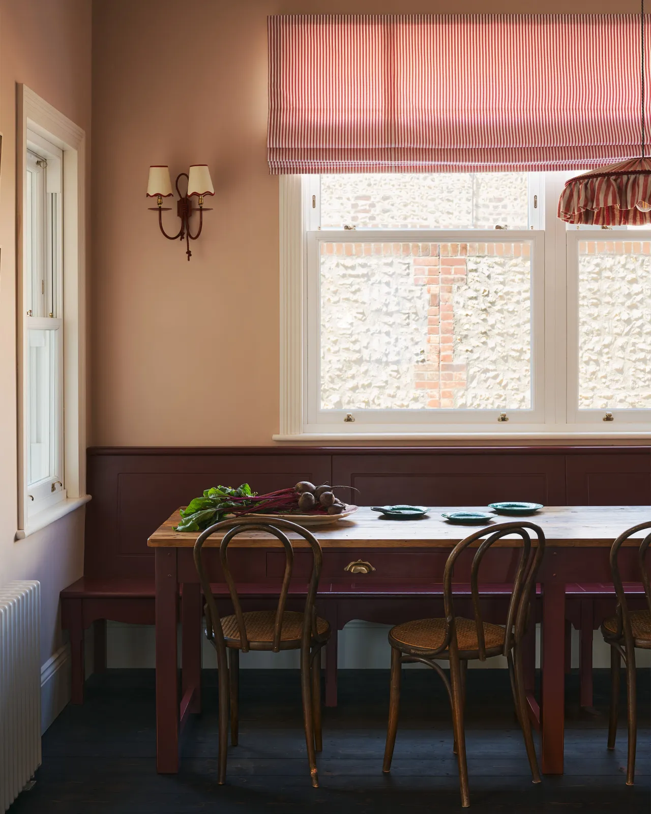 A straight-on view of a long banquet-style dining table with a reclaimed pine top and red painted frame and legs. A red painted fitted bench seat can be seen behind the table.