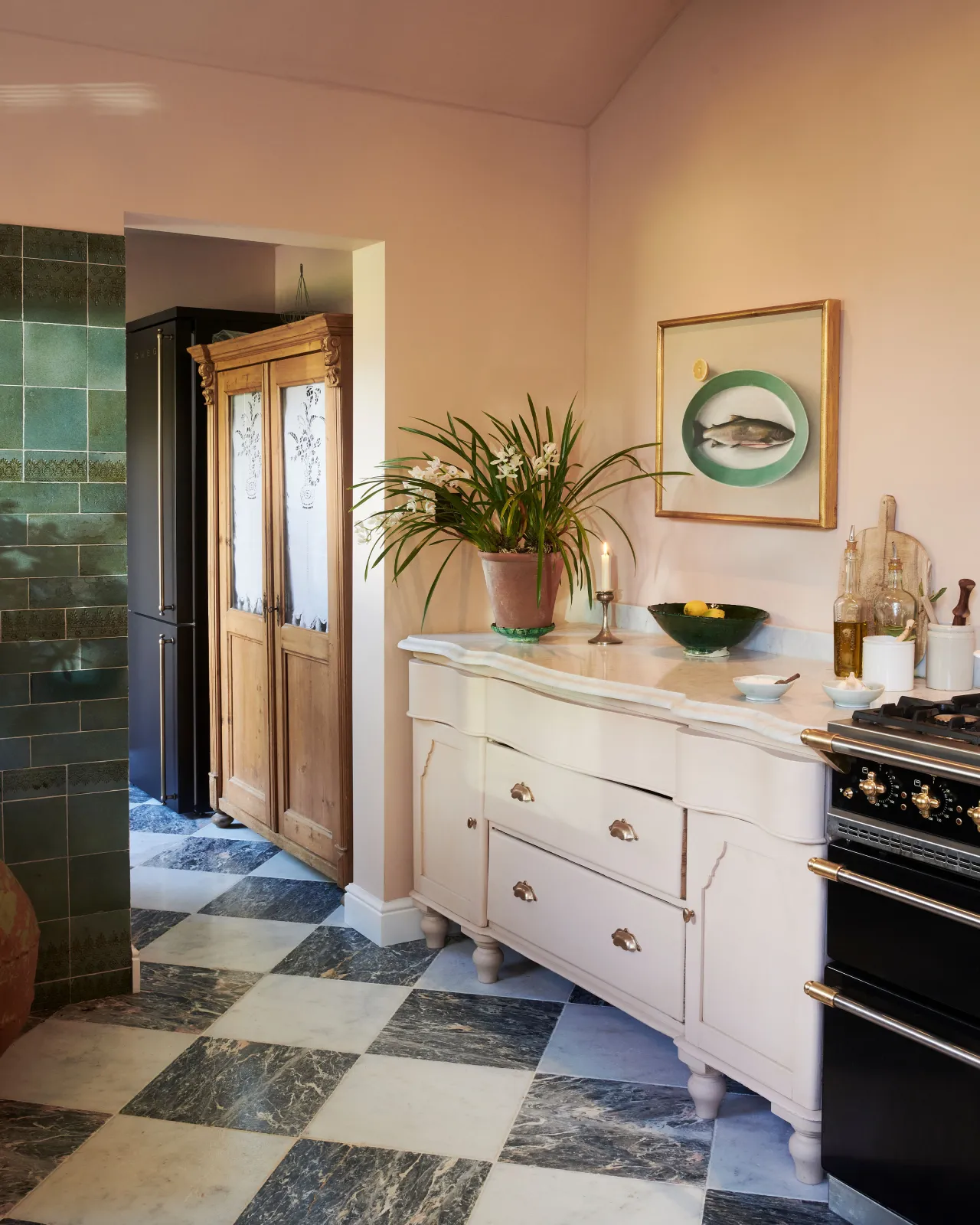 An oblique view of an antique door/drawer cabinet in an eclectic room with peach coloured walls, vintage styling, glossy teal wall tiles and a black and white chequered marble floor.