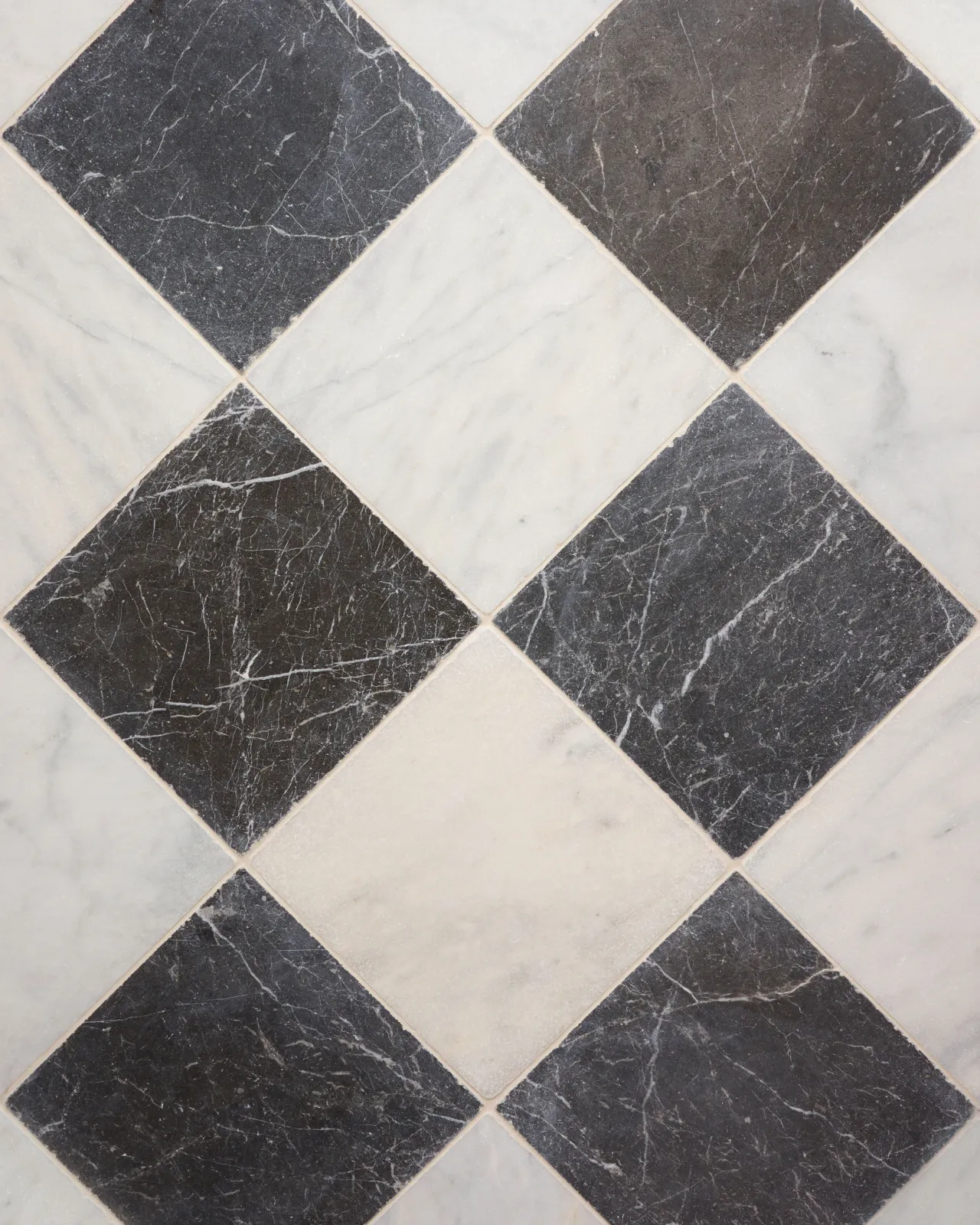 An overhead view of a black and white chequered marble floor, viewed with diagonal grout lines.
