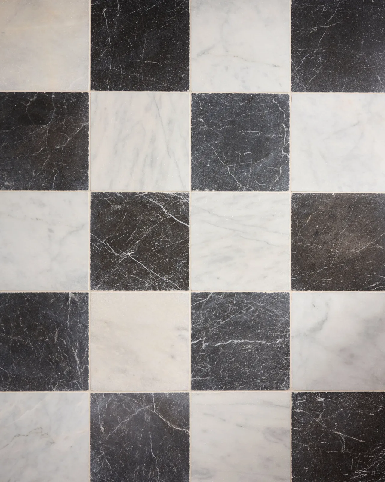 An overhead view of a black and white chequered marble floor, viewed with straight grout lines.