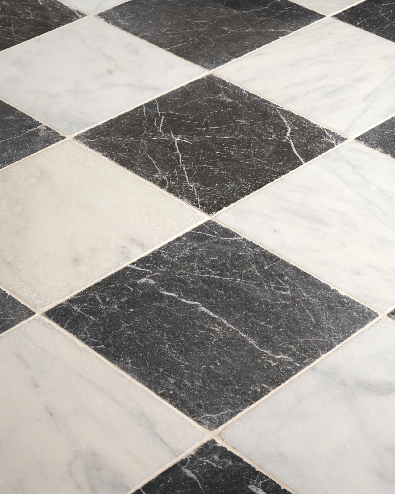 An oblique view of a black and white chequered marble floor, viewed with diagonal grout lines.