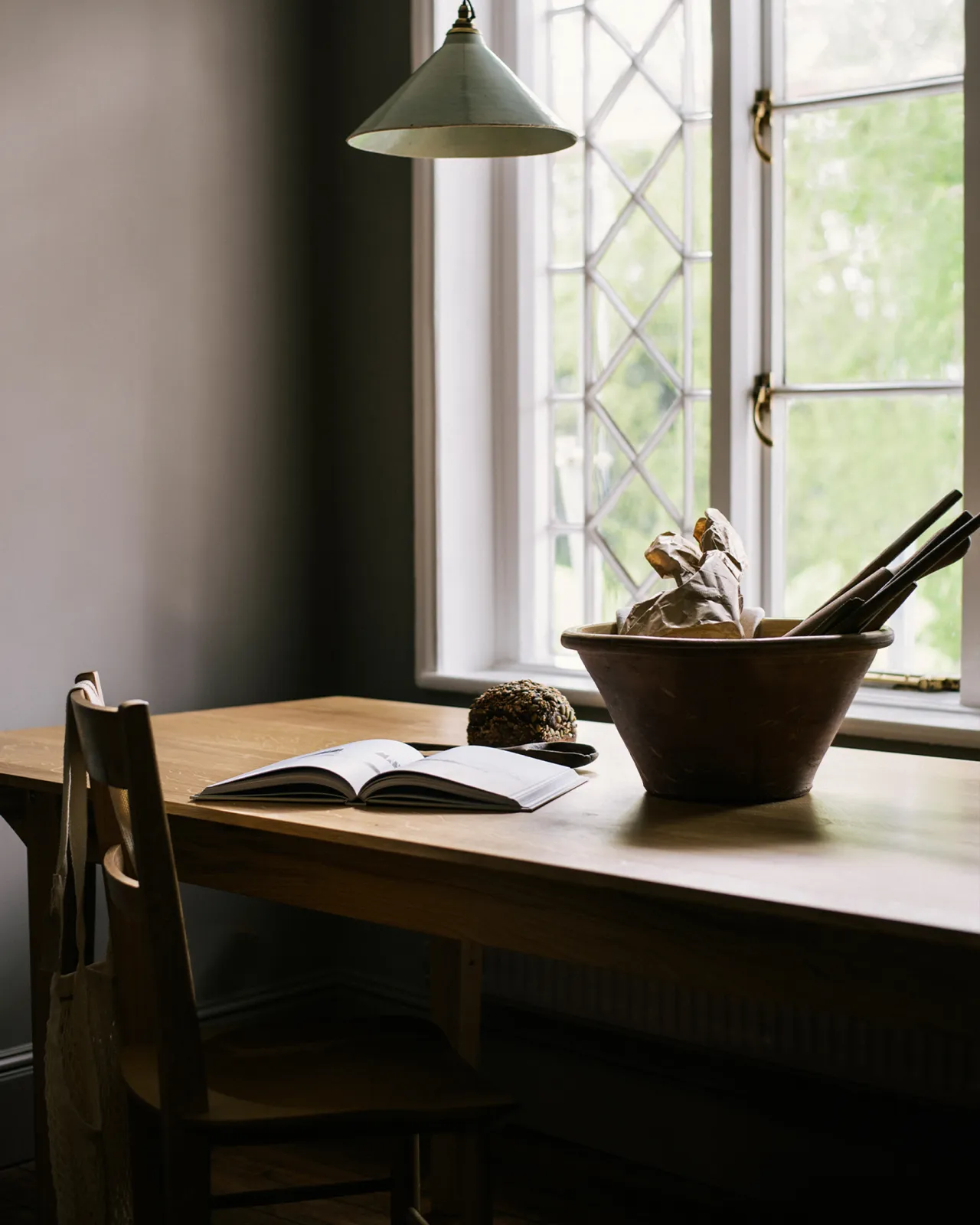 An oblique view of an oak tabletop with a large ceramic bowl in front of a Victorian leaded window.