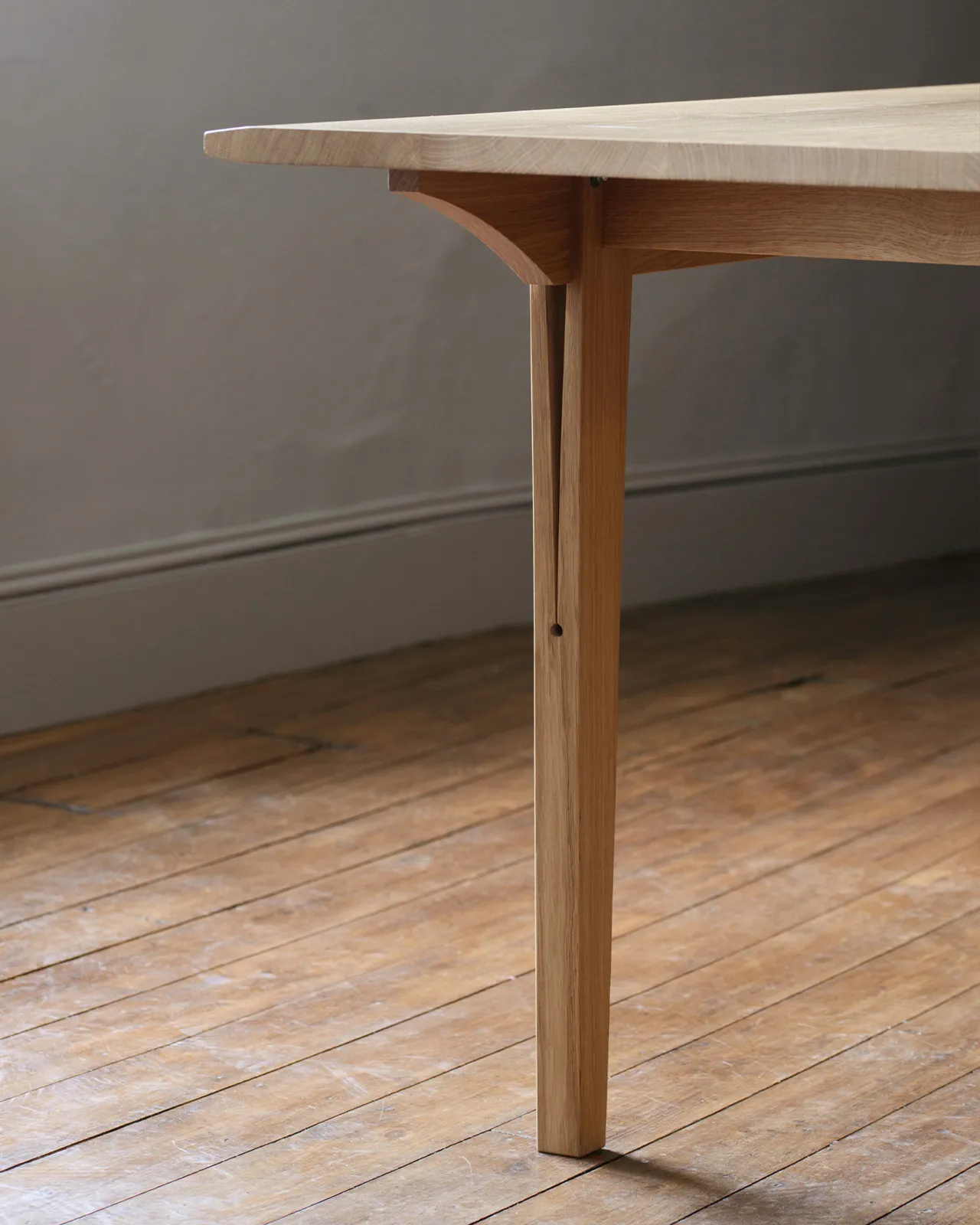 A close-up view of a chamfered oak table leg with a long split design which locks onto the table apron.