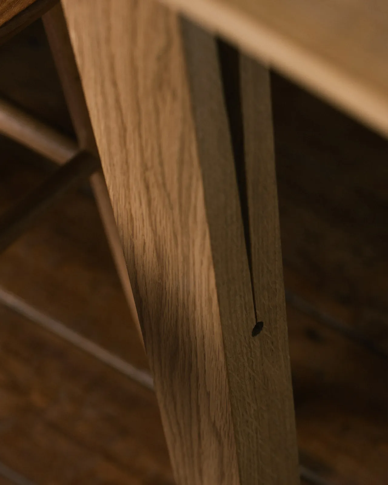A close-up oblique view of a chamfered oak table leg with a long split design which locks onto the table apron.