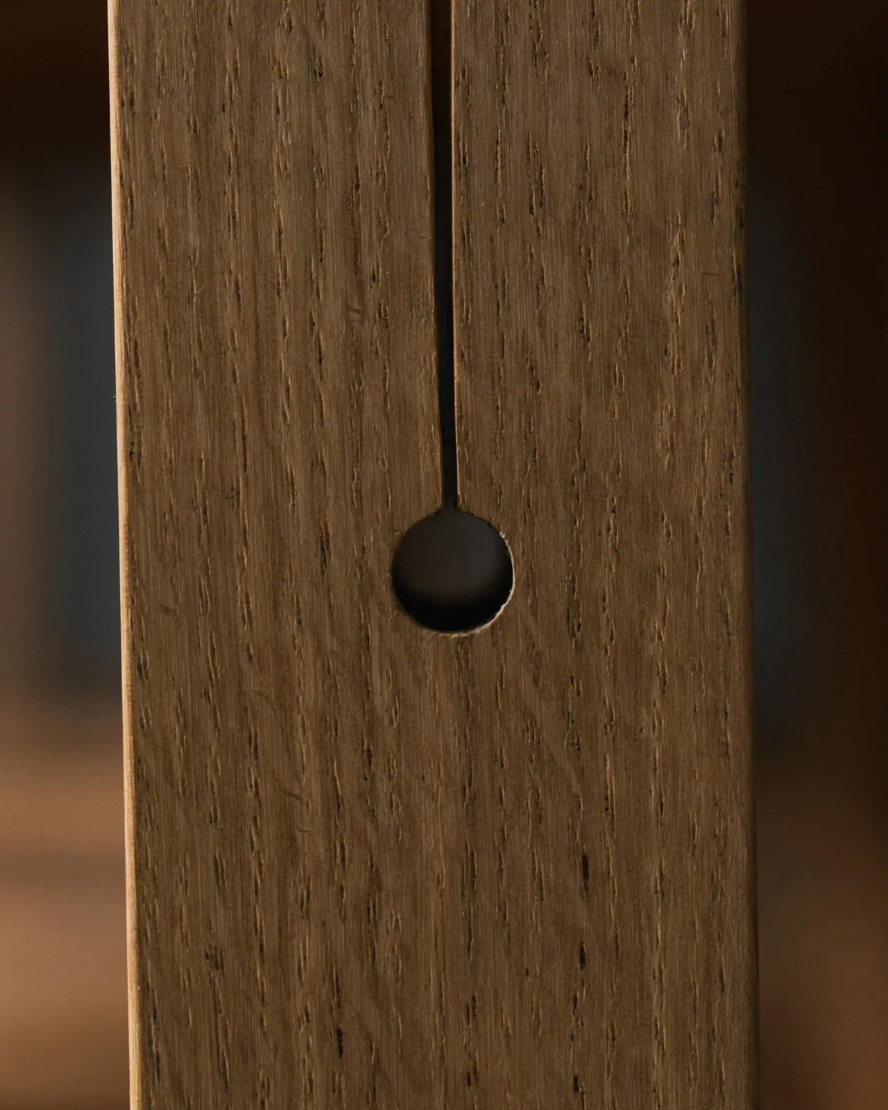 A close-up view of a circular hole at the base of a split design in an oak table leg.