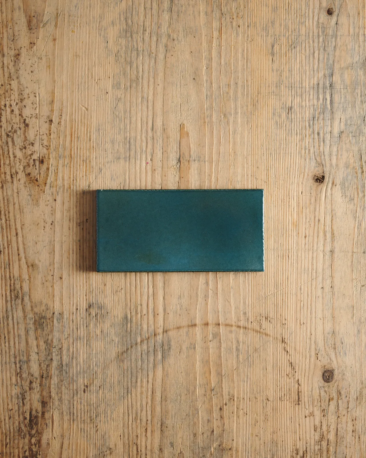 A glossy teal metro tile on a rustic wooden surface.